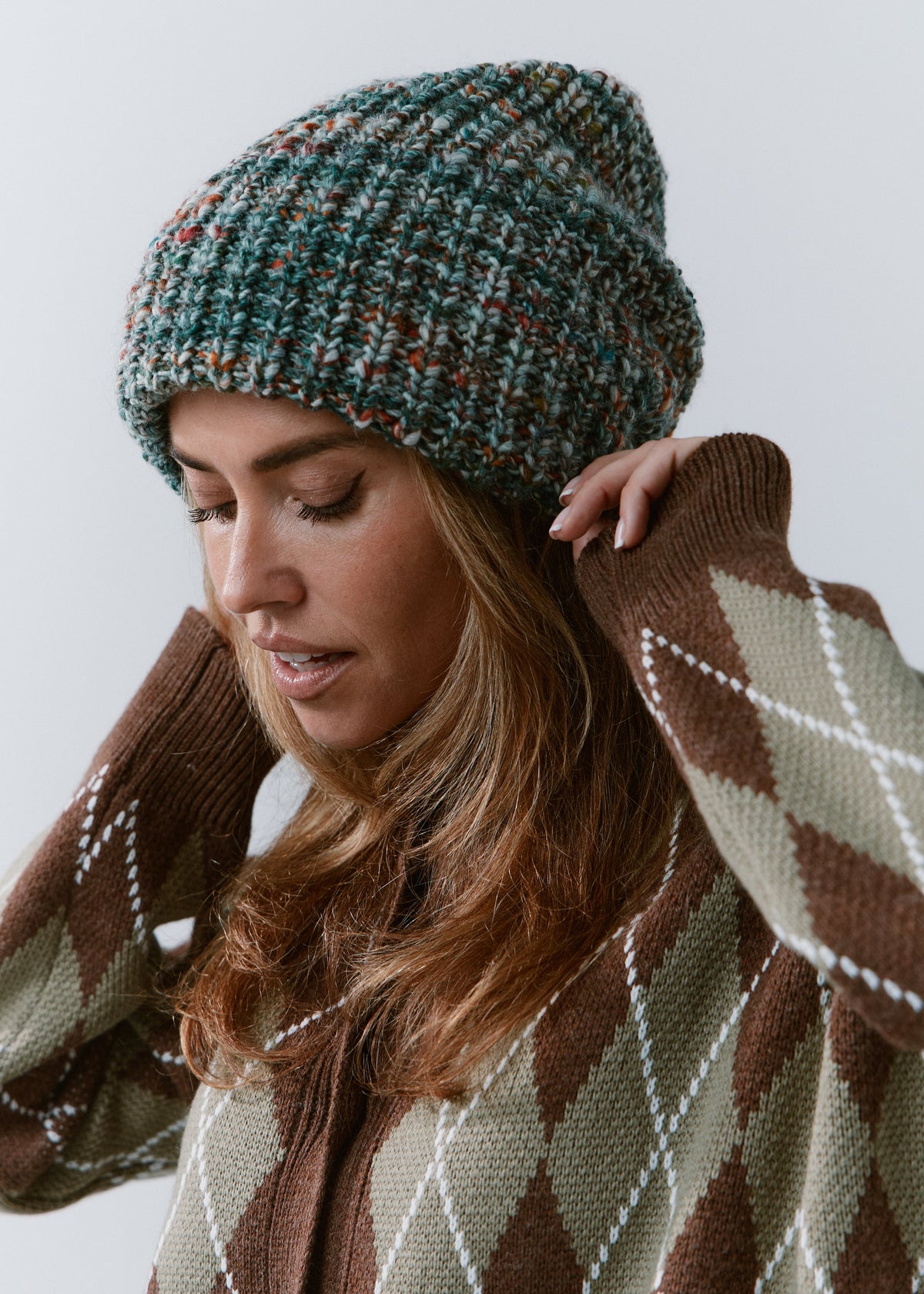 London Green and Orange knit beanie: Looking-down portrait with a hand beside the face
