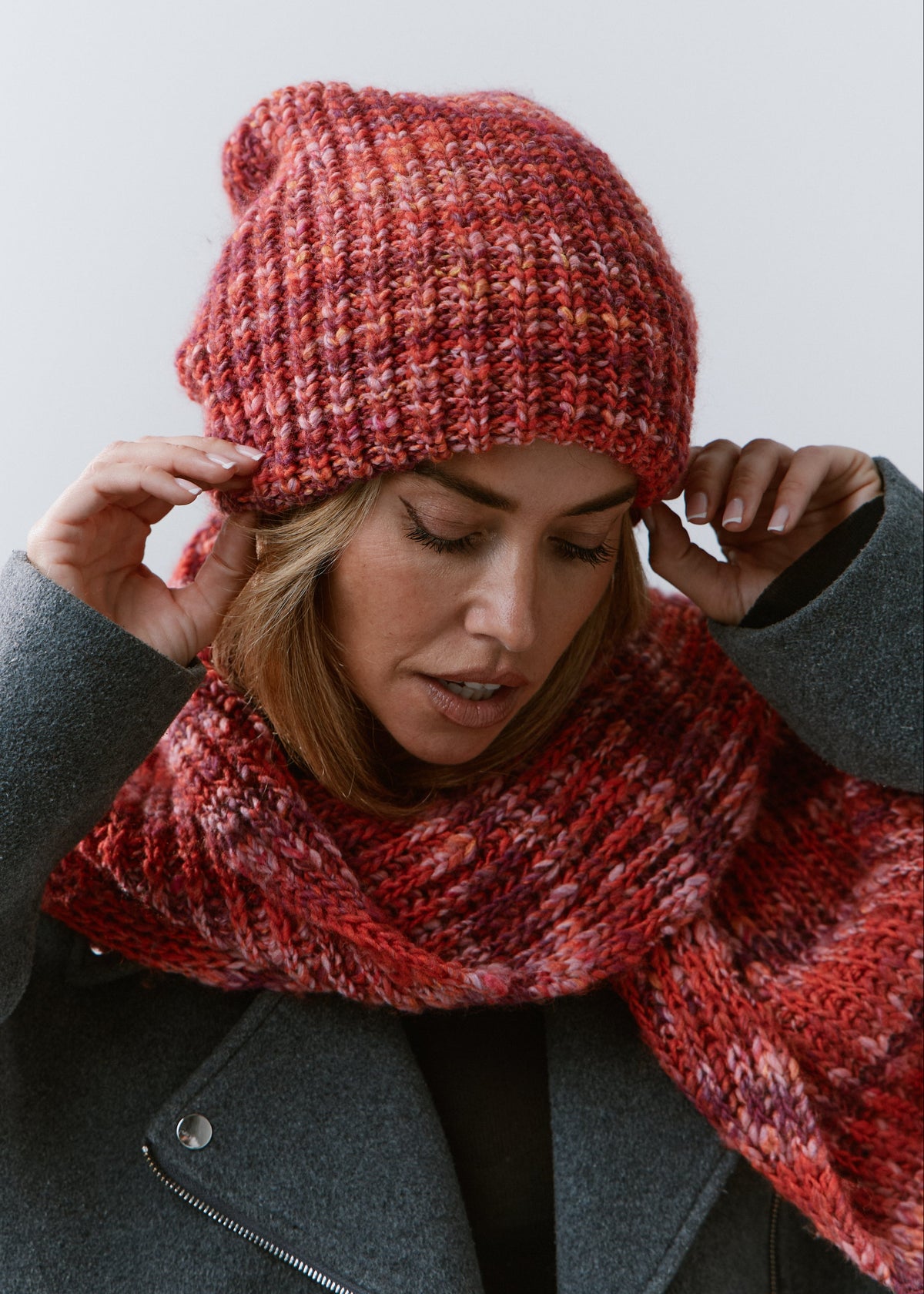 London Red knit beanie: Portrait with hands at the brim and matching scarf, sold separately