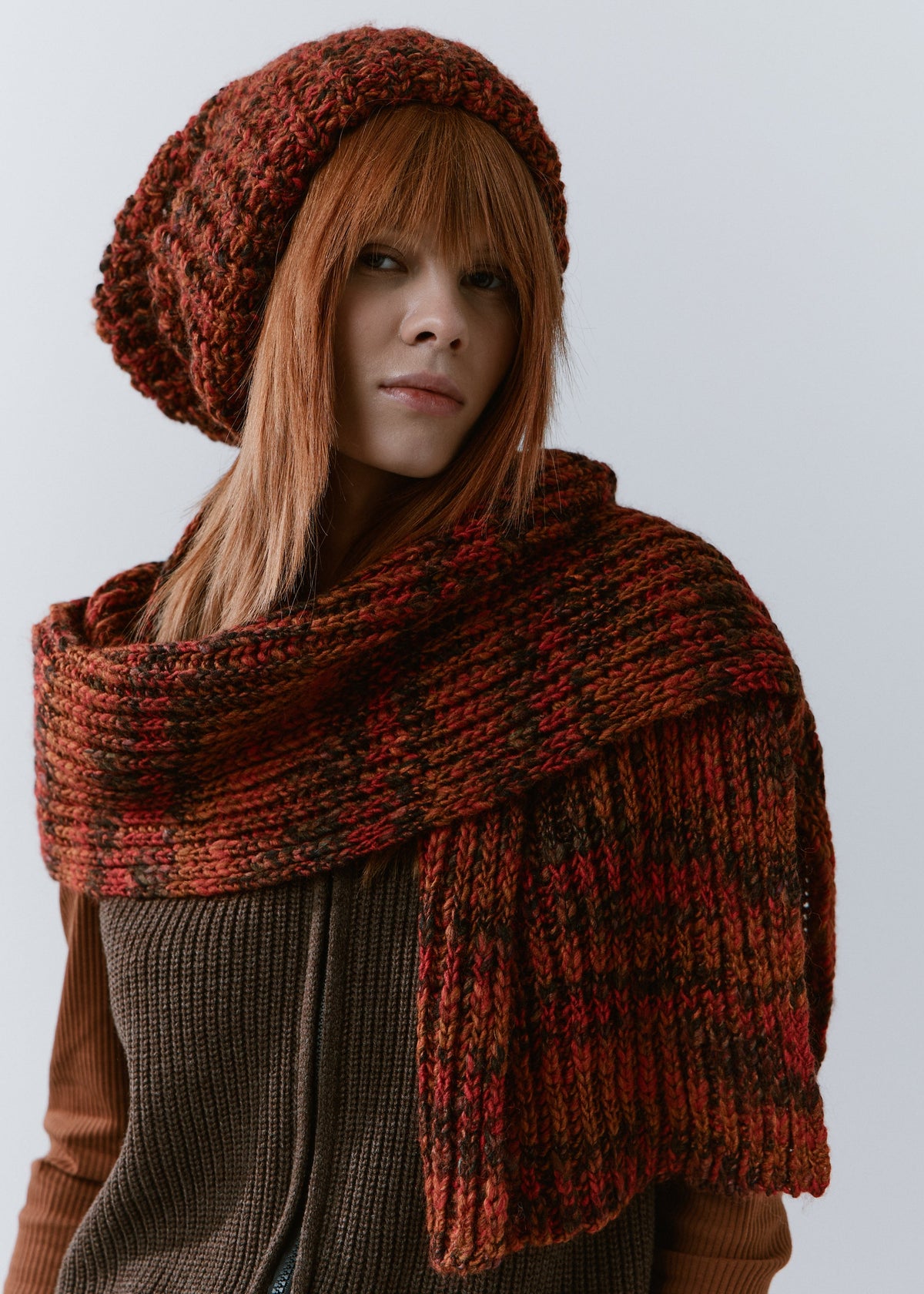 BRIKOLY Brown ribbed knit scarf in red-brown multicolor yarn, wrapped across a model's shoulders with one end hanging in front.