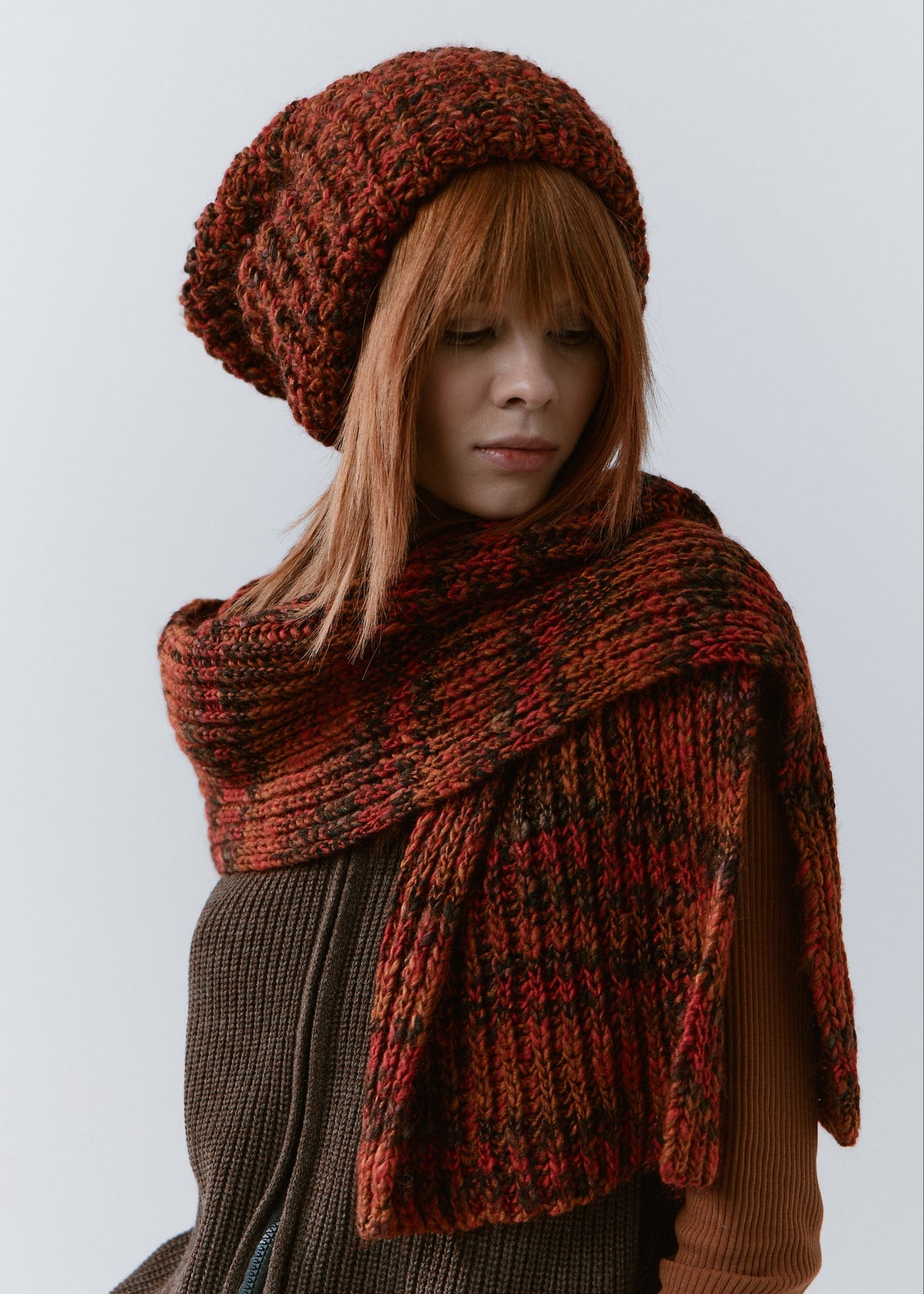 BRIKOLY Brown ribbed knit scarf in red-brown multicolor yarn, worn by a model looking down, showing its ribbed texture.