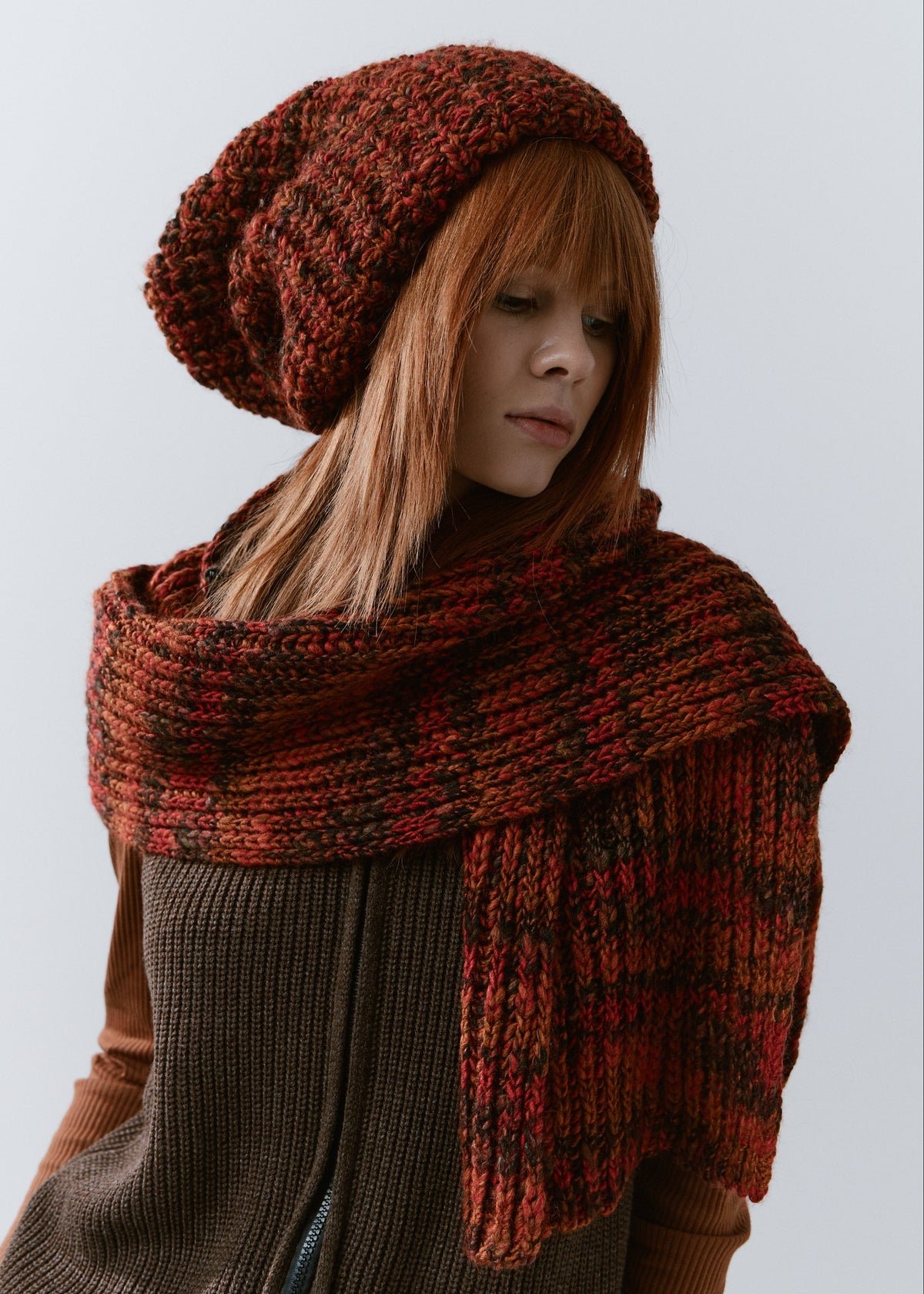 BRIKOLY Brown ribbed knit scarf in red-brown multicolor yarn, worn by a model looking to the side with one end hanging down.