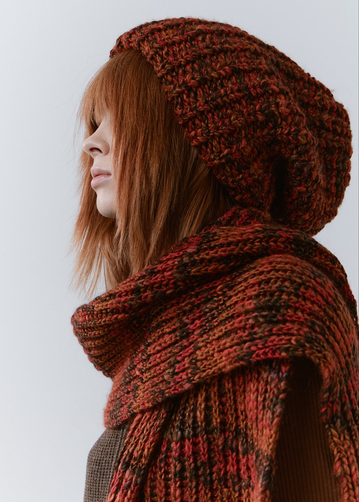 BRIKOLY Brown ribbed knit scarf in red-brown multicolor yarn, wrapped across a model's shoulders in a close side view.