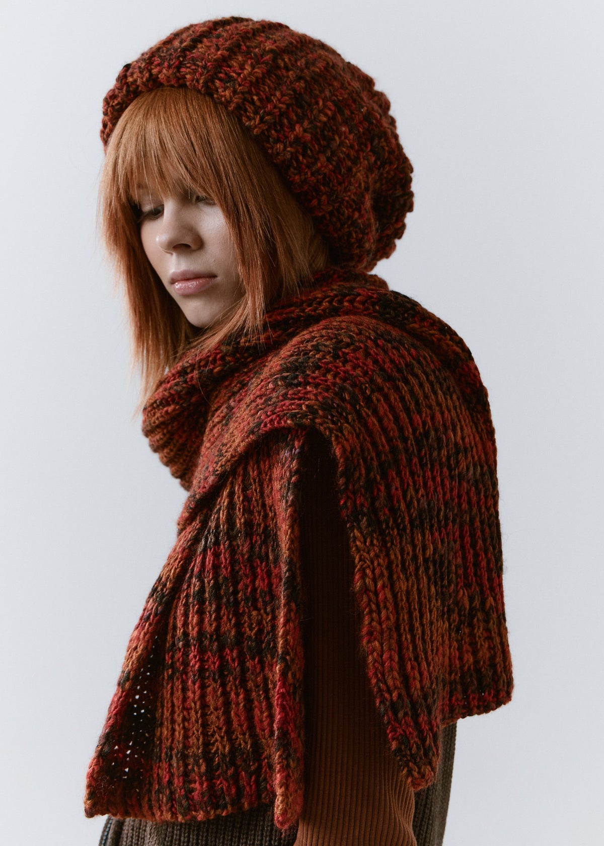BRIKOLY Brown ribbed knit scarf in red-brown multicolor yarn, draped over a model's shoulder in a rear three-quarter view.