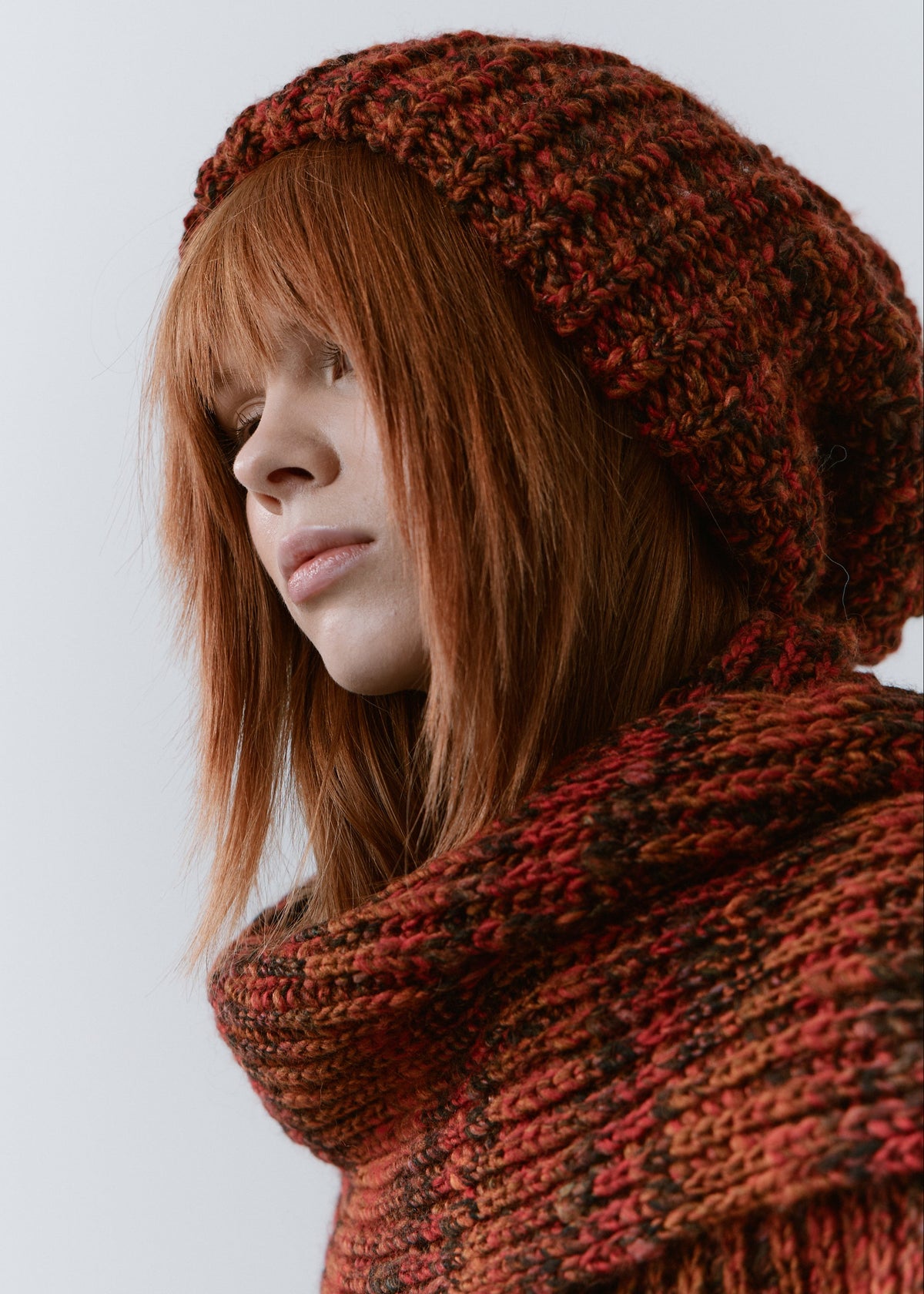 BRIKOLY Brown ribbed knit scarf in red-brown multicolor yarn, shown close up around a model's neck in profile.
