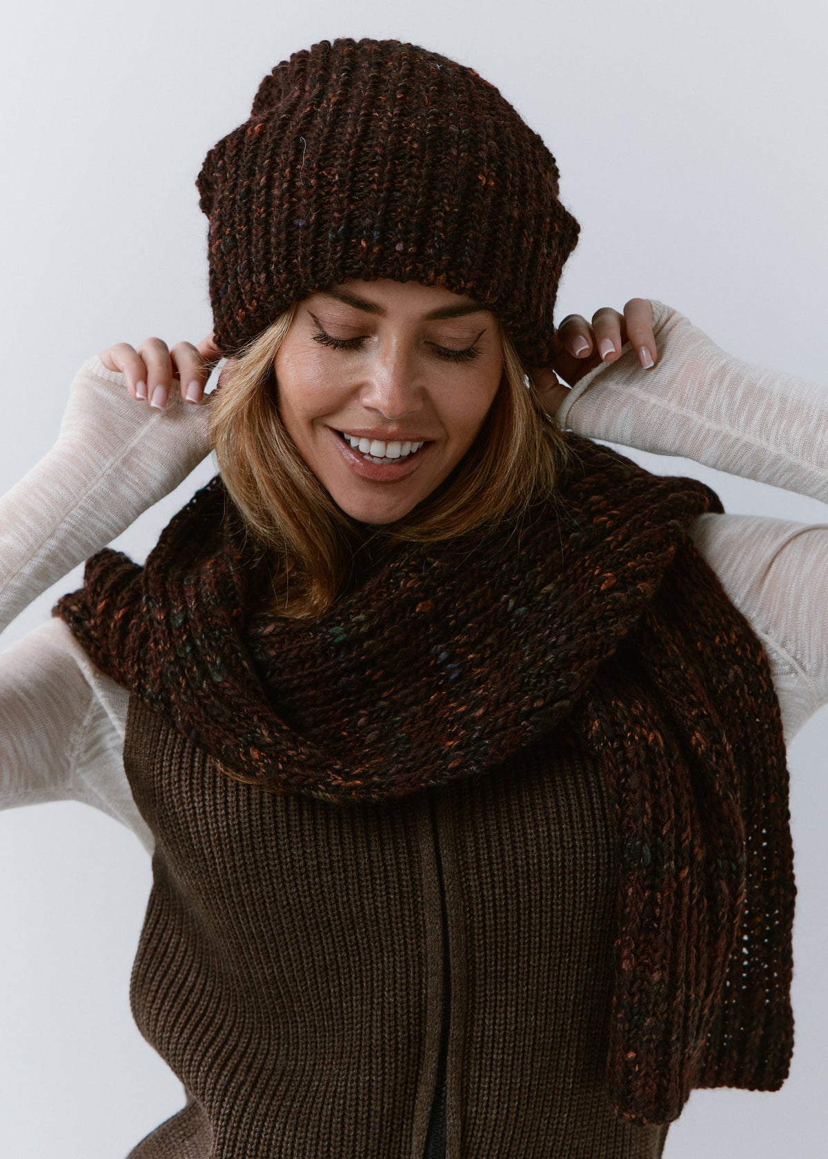 London Burgundy and Black knit beanie: Smiling portrait with matching scarf and hands at the brim, sold separately