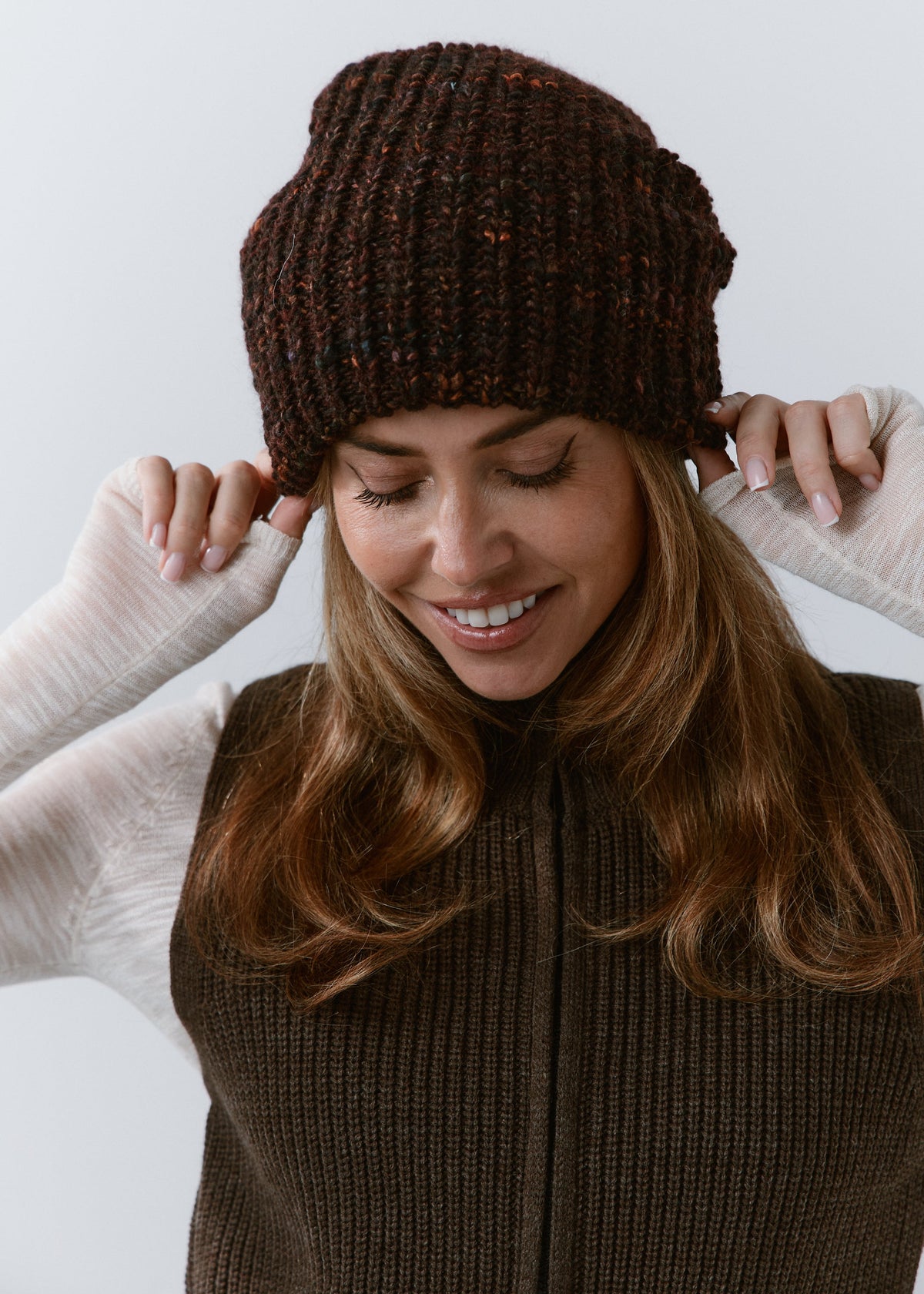 London Burgundy and Black knit beanie: Smiling portrait with hands at the brim