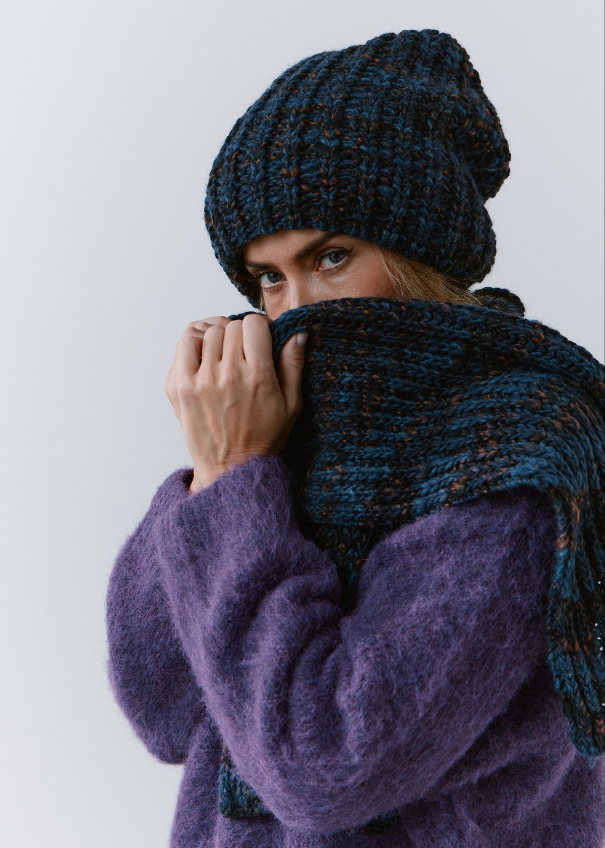 BRIKOLY Dark Lavender ribbed knit scarf in dark blue multicolor yarn, held up near a model's face to show its chunky knit texture.