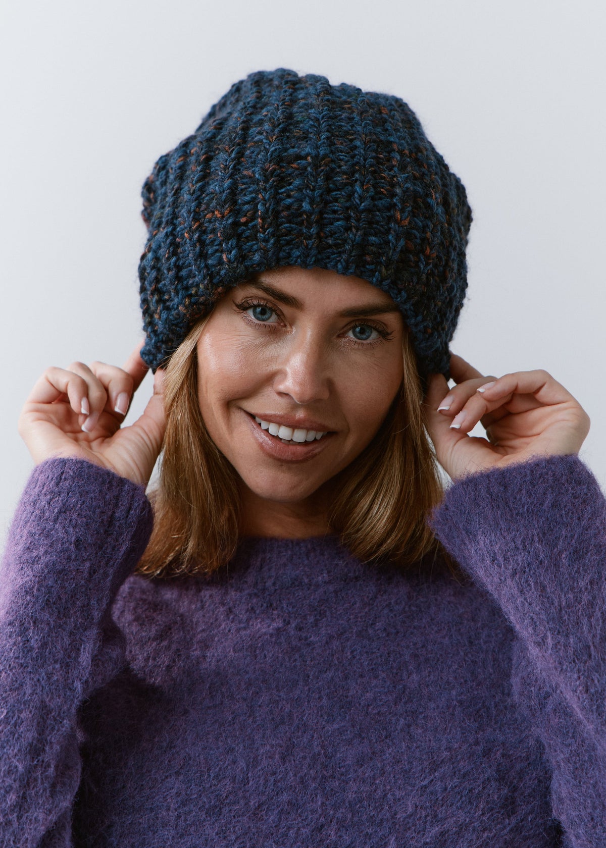 BRIKOLY Dark Lavender oversized knit beanie worn by a smiling model adjusting the brim.