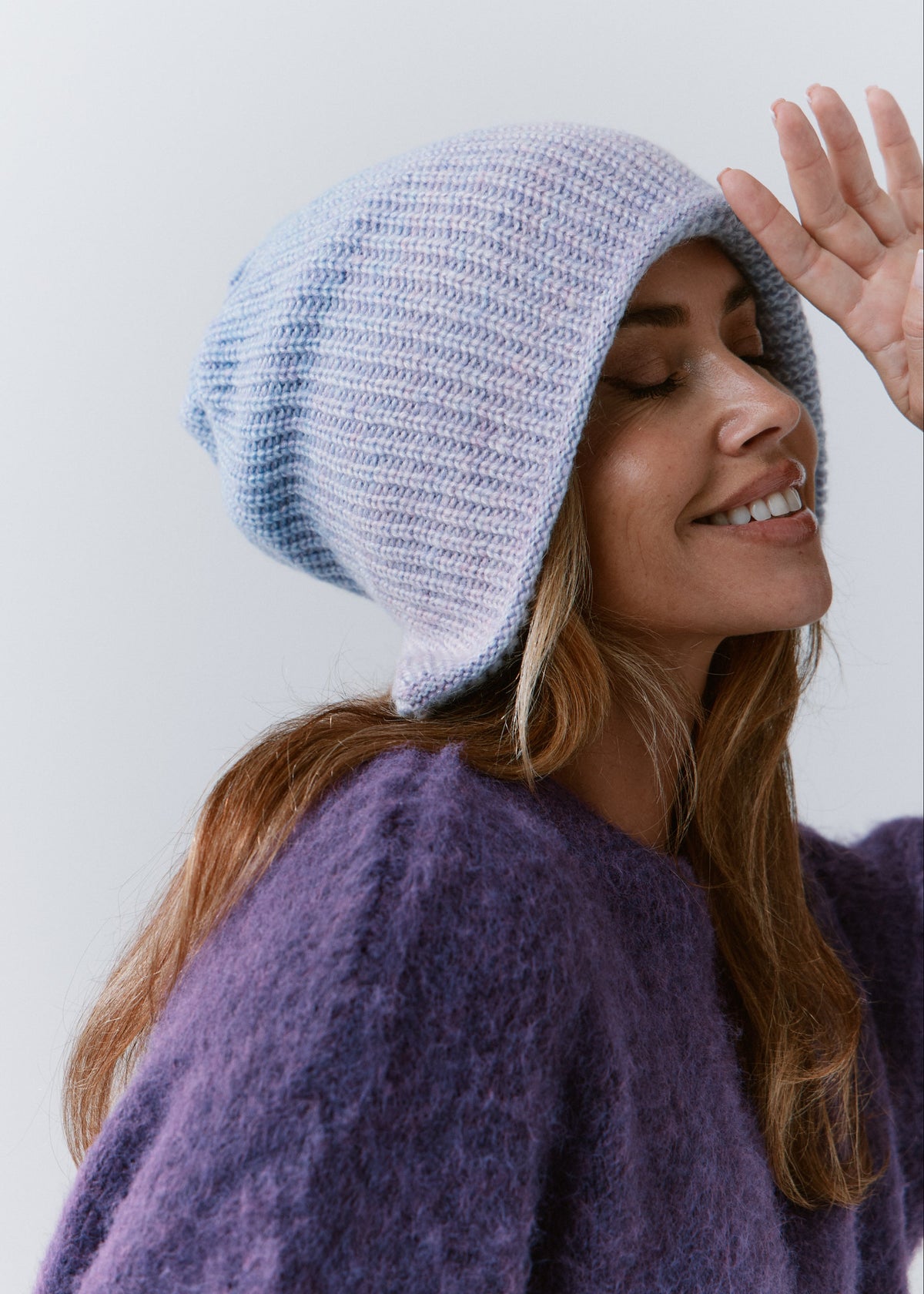 BRIKOLY Lisse Pink reversible knit beanie in pale blue and lilac tones, shown in profile on a smiling model.