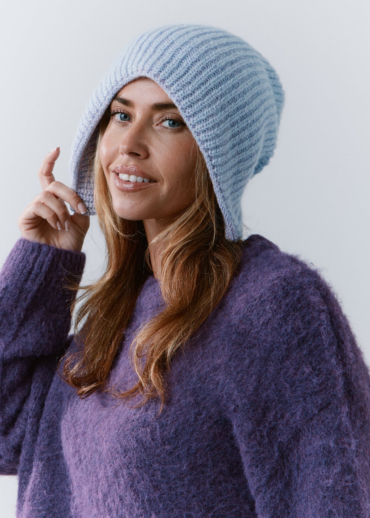 BRIKOLY Lisse Pink reversible knit beanie in pale blue and lilac tones, shown on a smiling model in a three-quarter view.