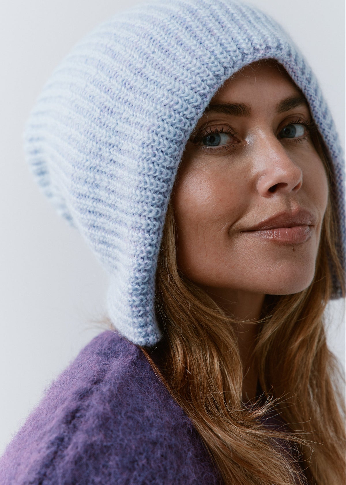 BRIKOLY Lisse Pink reversible knit beanie in pale blue and lilac tones, shown close up on a model looking toward the camera.