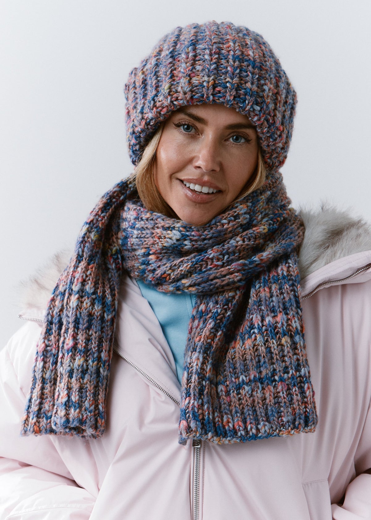 Front view of the BRIKOLY Pink Blue multicolor knit scarf styled with a matching beanie and light pink jacket.