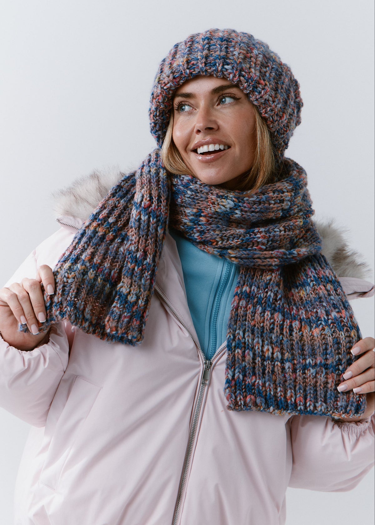 Model holding the ends of the BRIKOLY Pink Blue scarf to show its ribbed texture and multicolor yarn.