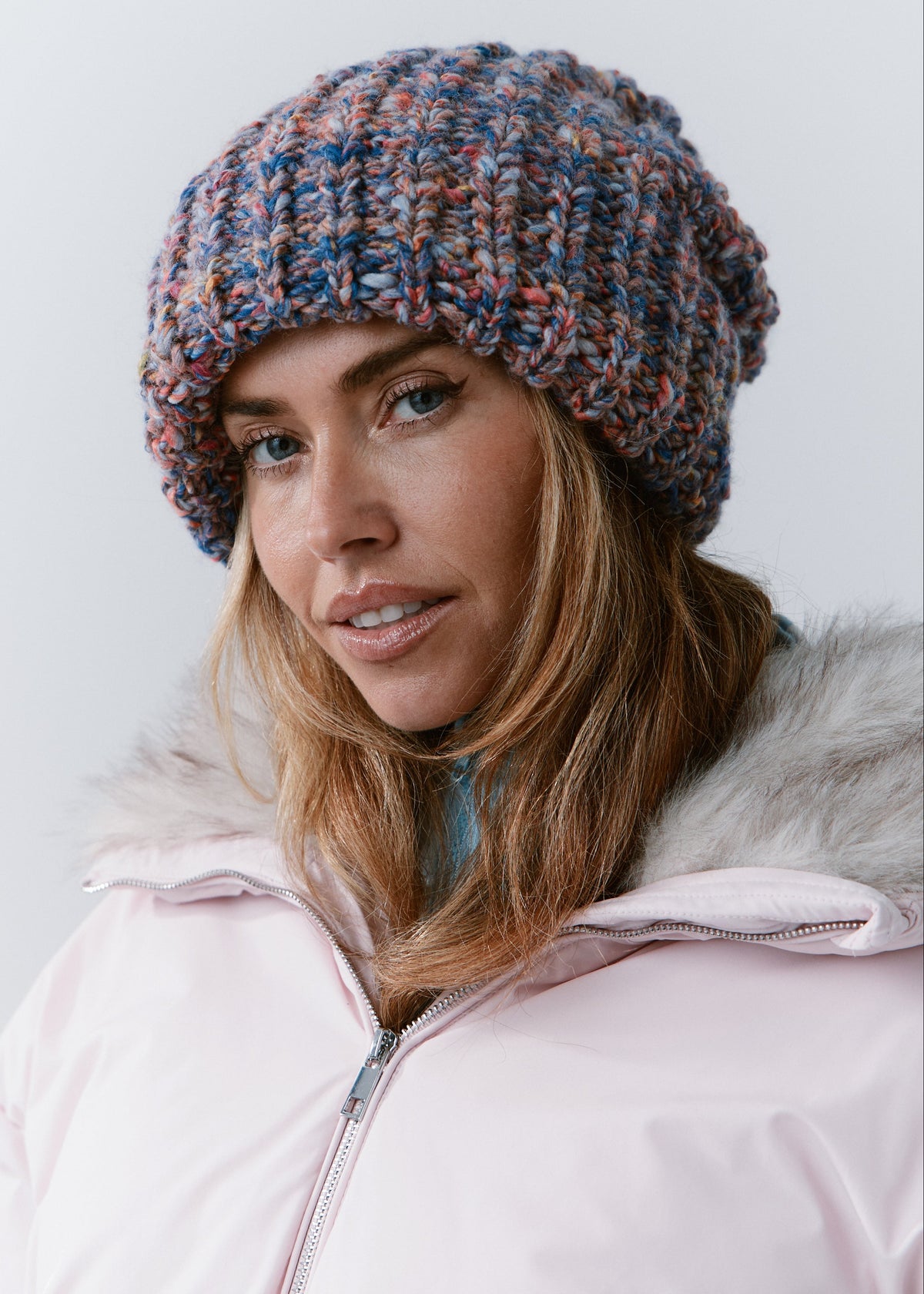 BRIKOLY Pink Blue oversized multicolor knit beanie shown in a front view over a light pink winter jacket.