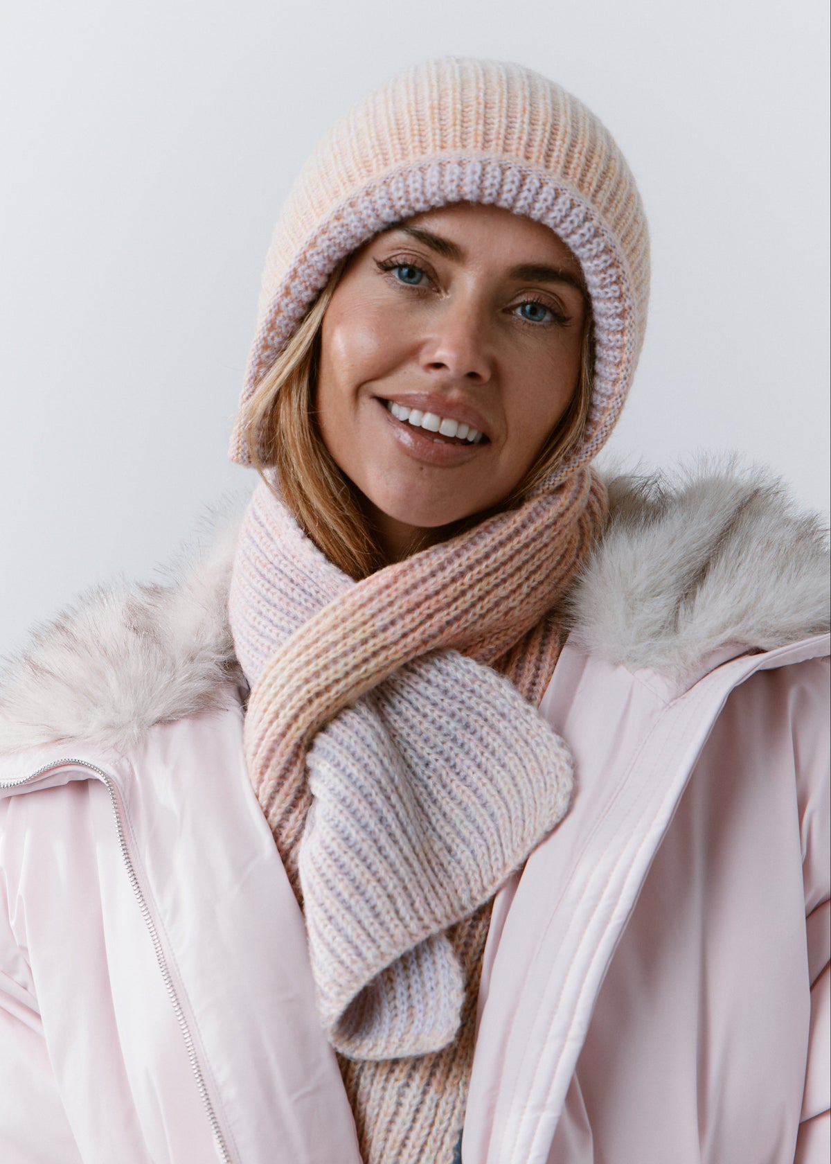 BRIKOLY Lisse Unicorn reversible ribbed knit beanie worn on its pale peach side by a model with a matching scarf.