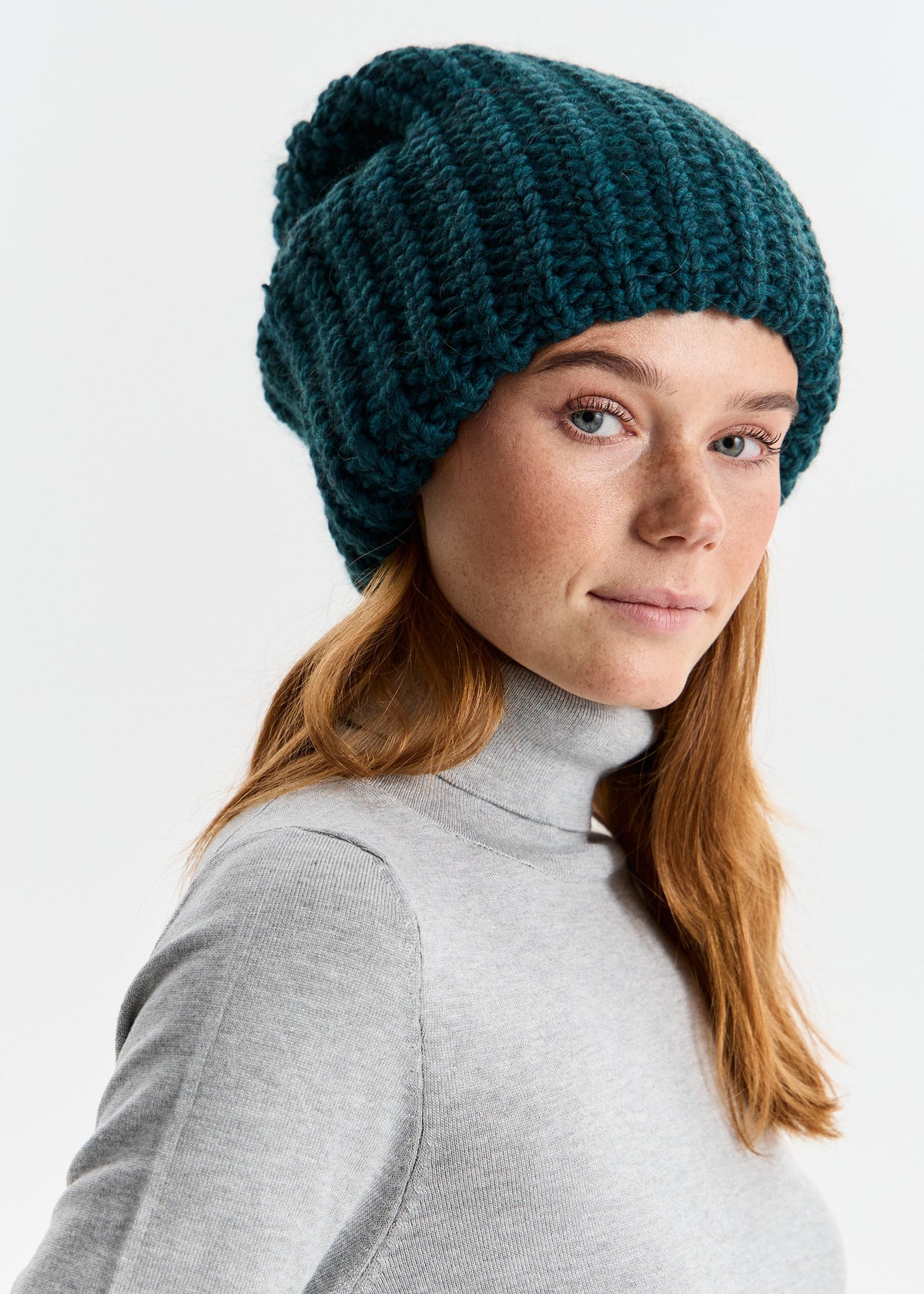 BRIKOLY London Emerald knit beanie shown on a model looking back in a gray top.