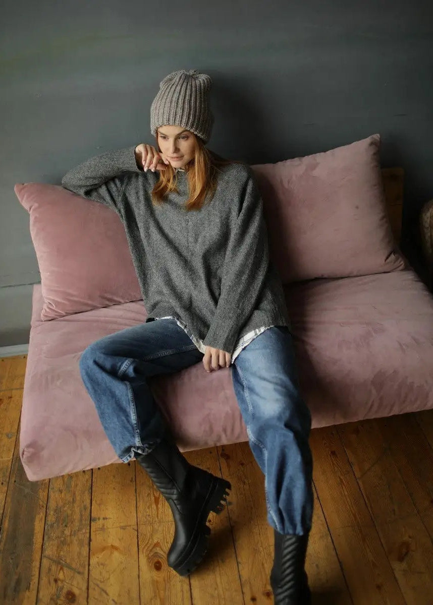 BRIKOLY London Gray & Beige knit beanie shown on a model leaning against a sofa.