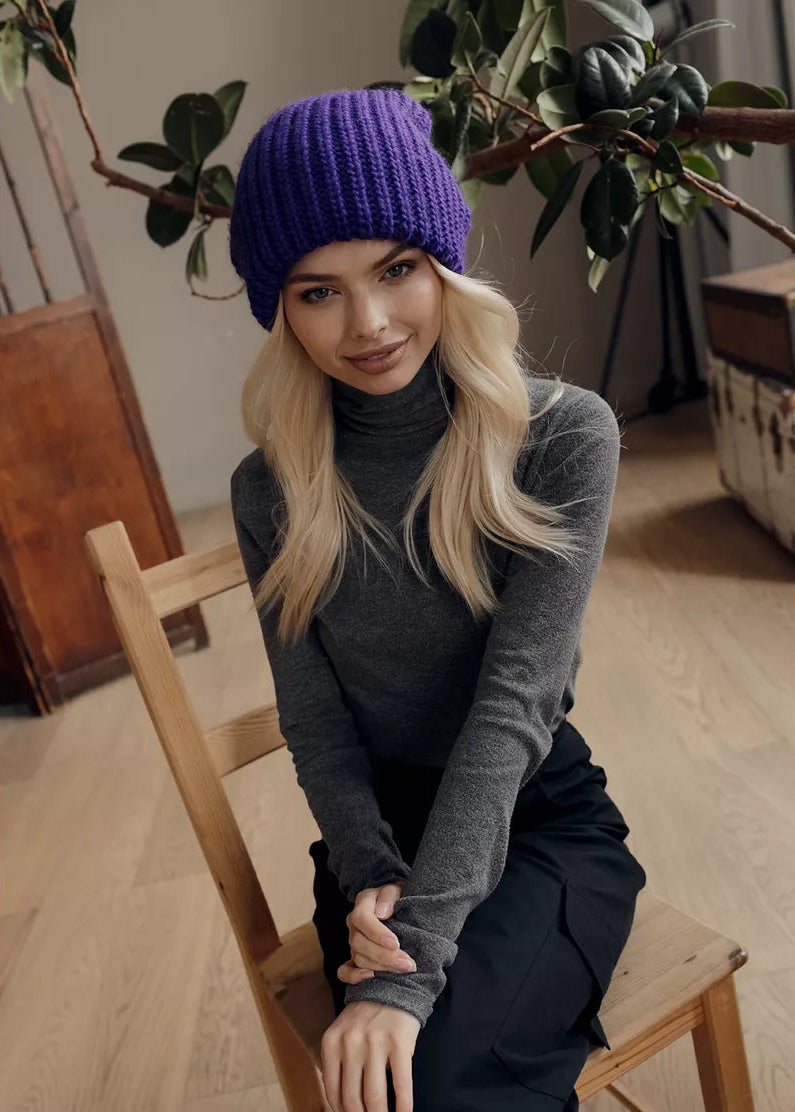 BRIKOLY London Lavender knit beanie shown on a seated model leaning toward the camera.