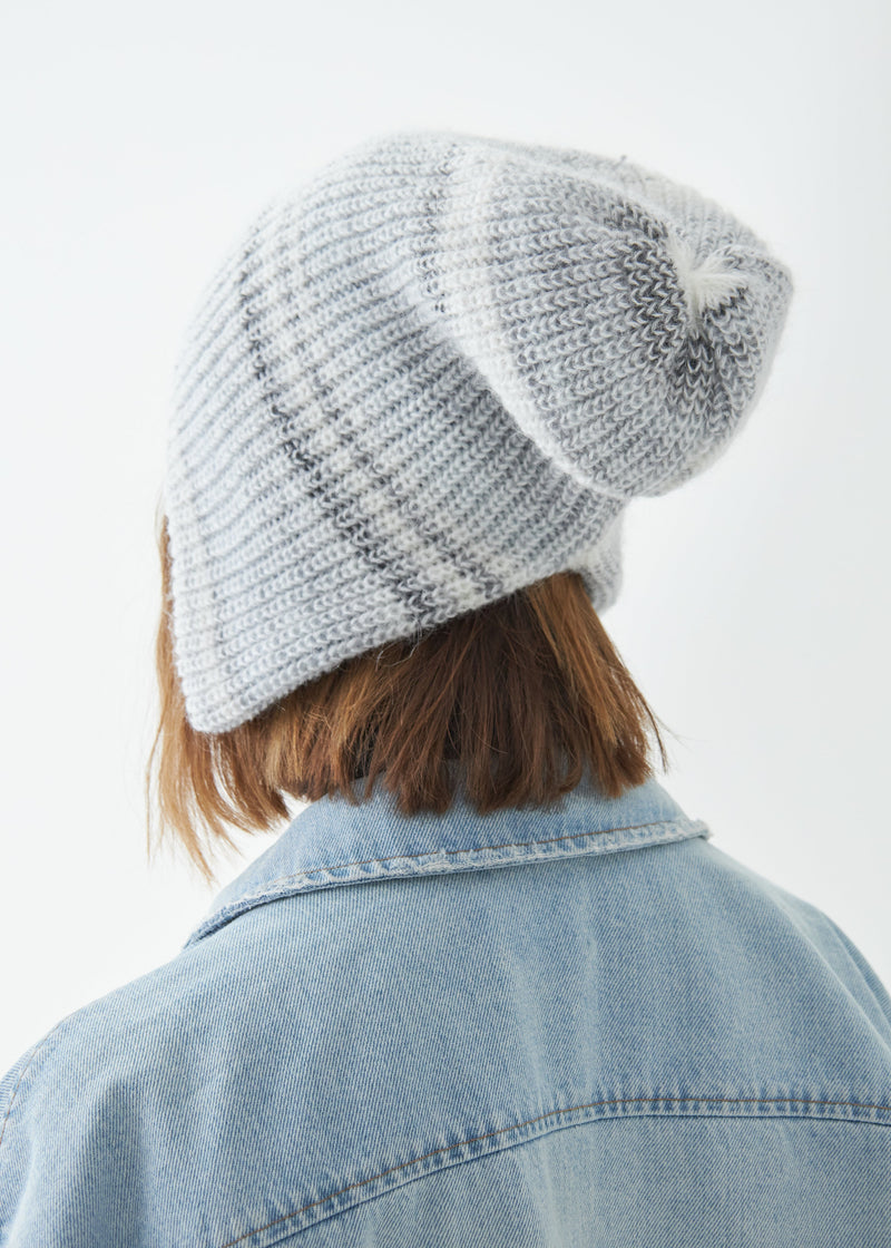 Person wearing a light gray knit beanie and denim jacket on a white background