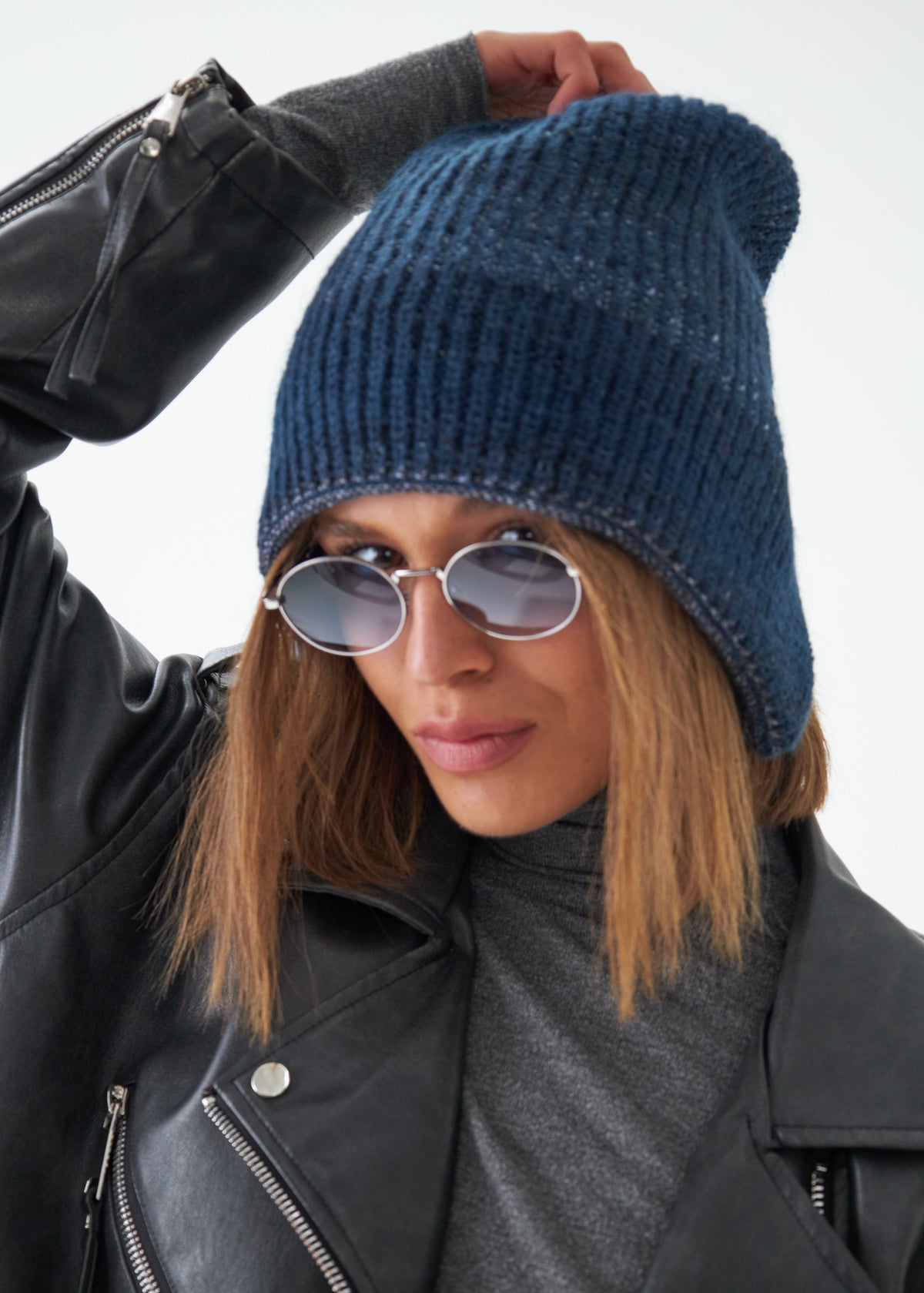 Person wearing a blue knit beanie and sunglasses with a black leather jacket.