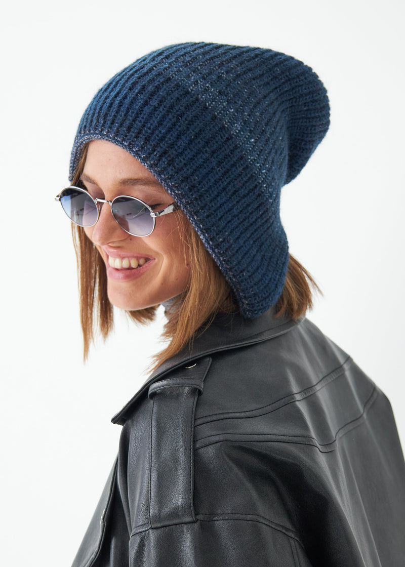 Woman wearing a blue knit beanie and sunglasses on a white background