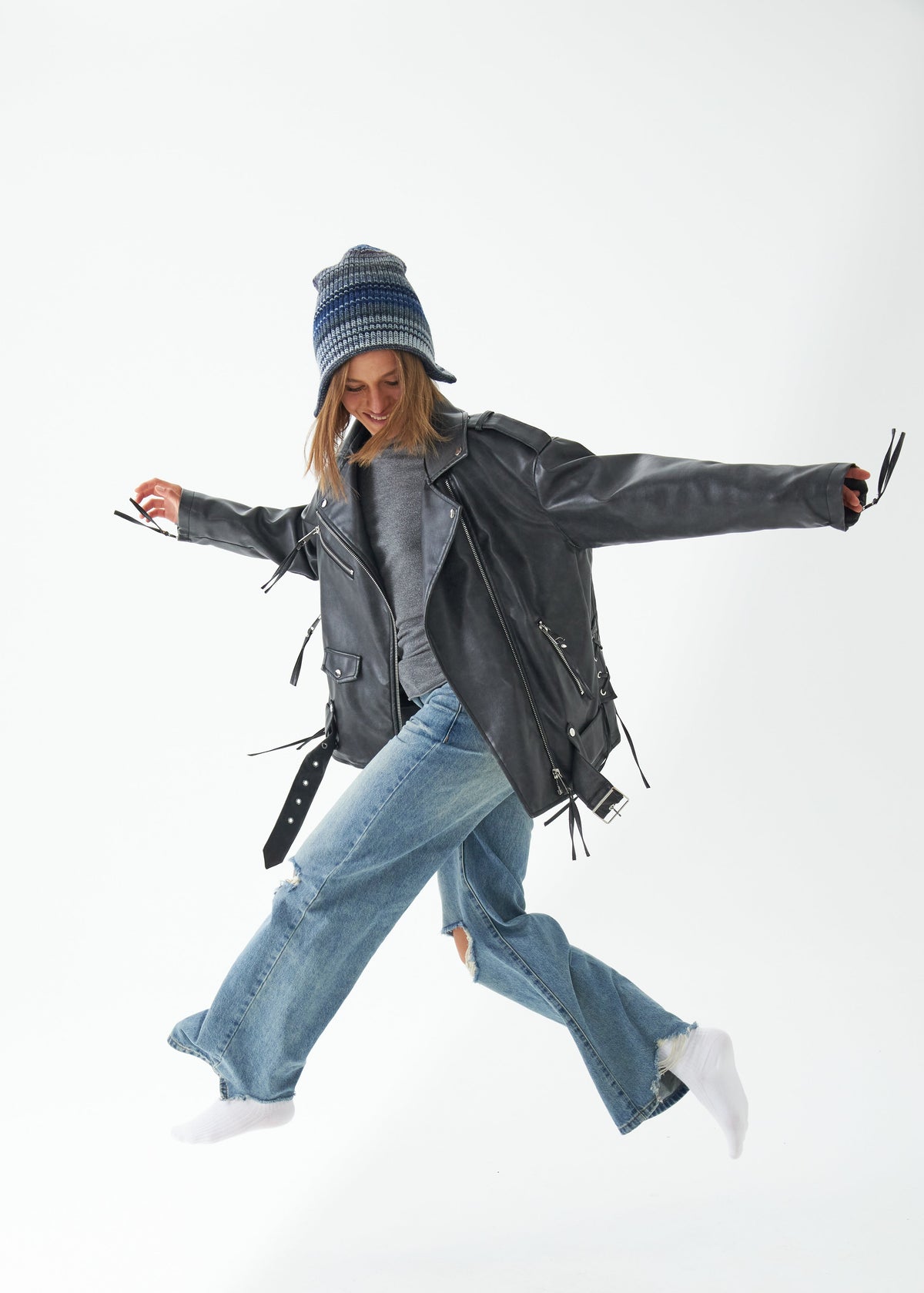 Person wearing a black leather jacket, blue jeans, and a patterned beanie on a white background