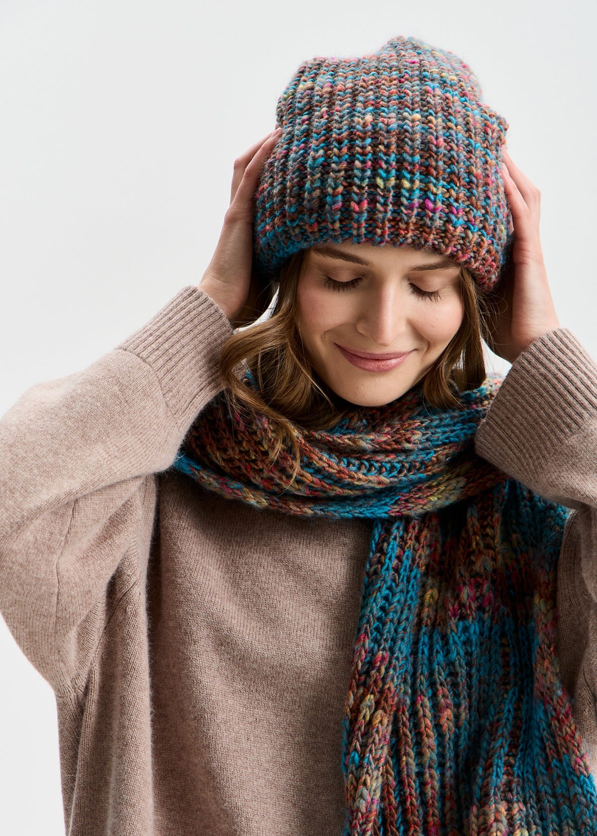 BRIKOLY London Turquoise multicolor knit beanie worn by a model adjusting the brim with a matching scarf.