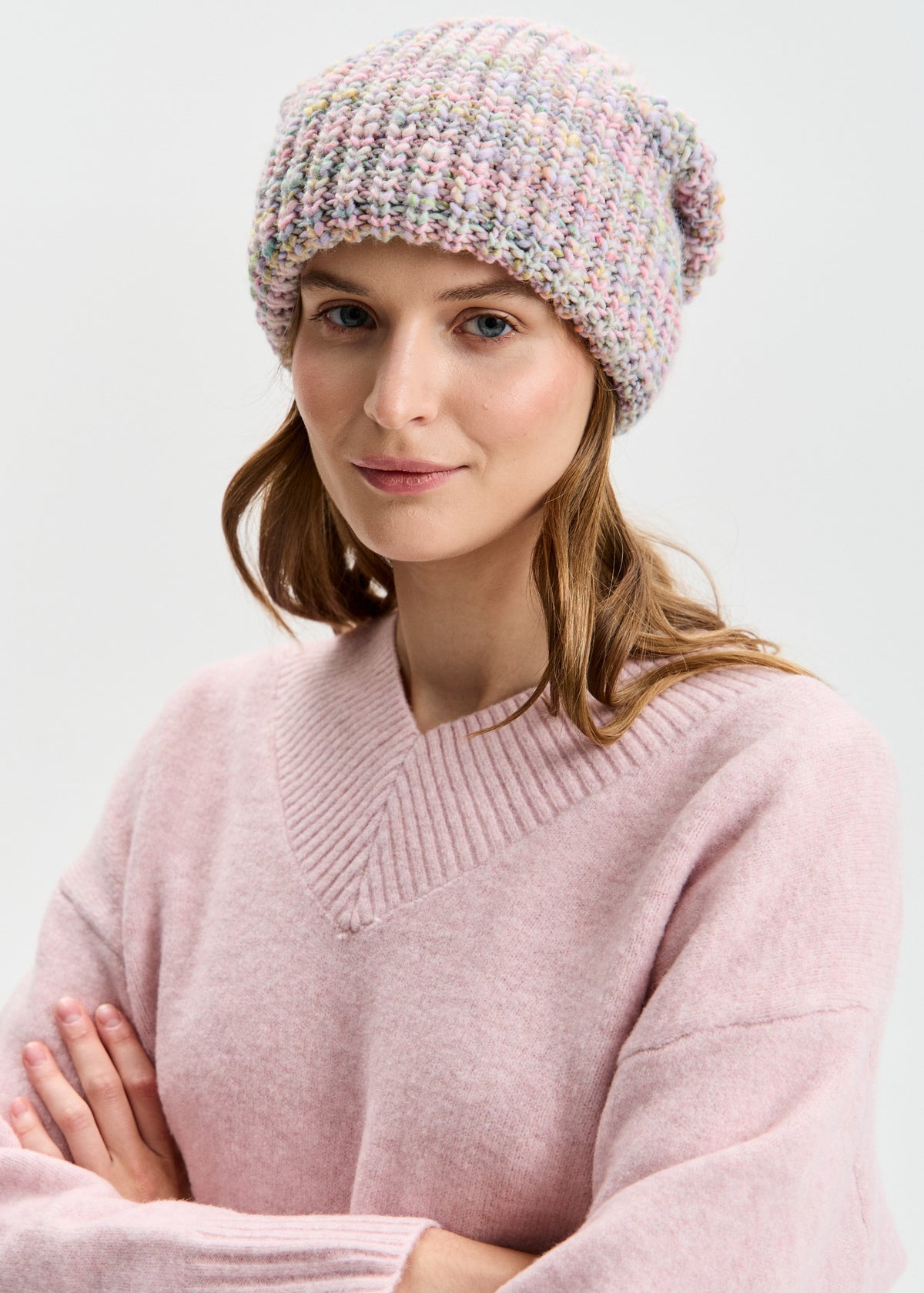BRIKOLY London Unicorn pastel multicolor knit beanie worn by a model with arms crossed.