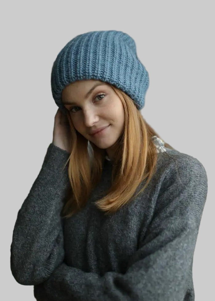 Woman wearing a blue knit beanie and gray sweater indoors