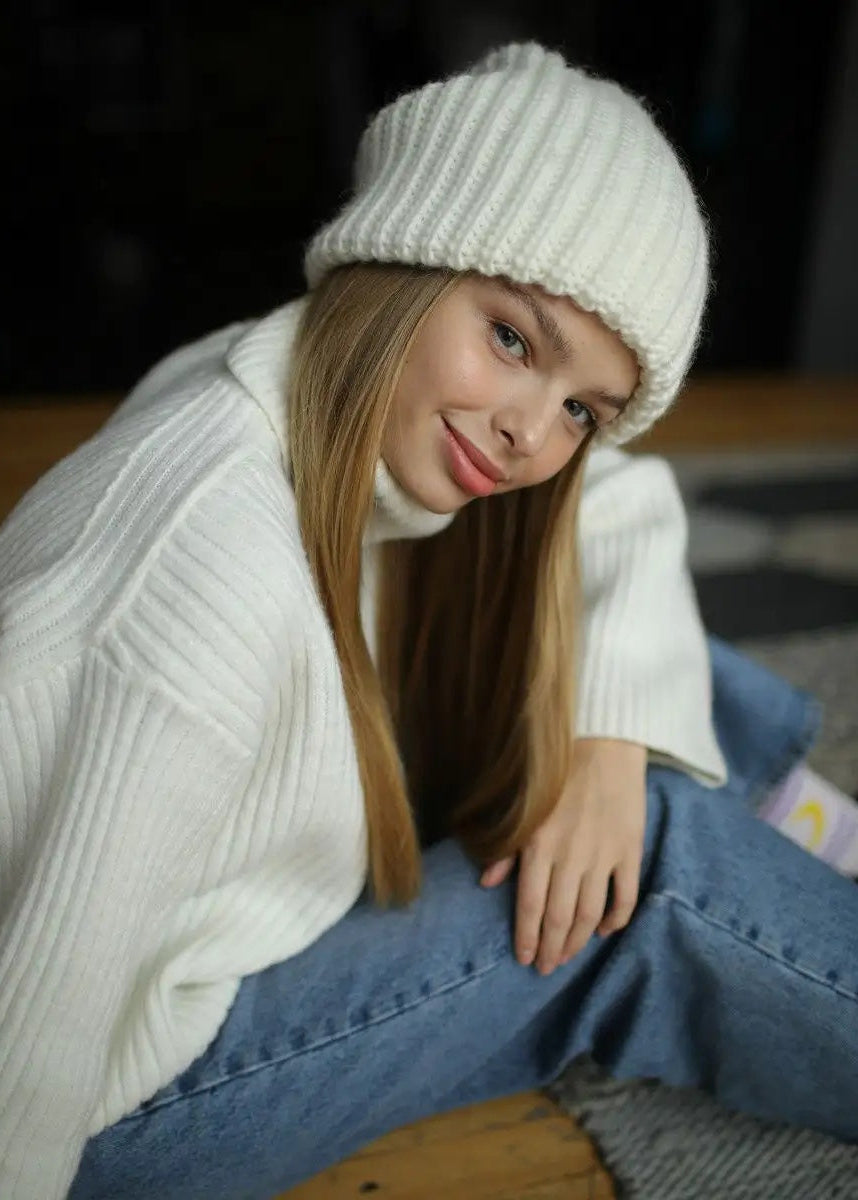BRIKOLY London White knit beanie shown on a model seated on the floor.