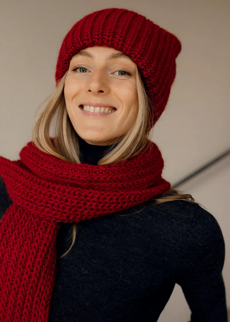 BRIKOLY London Burgundy knit beanie worn by a smiling model with a matching scarf.