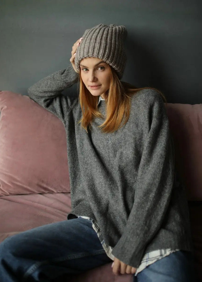 BRIKOLY London Gray & Beige knit beanie shown on a seated model adjusting the sides.