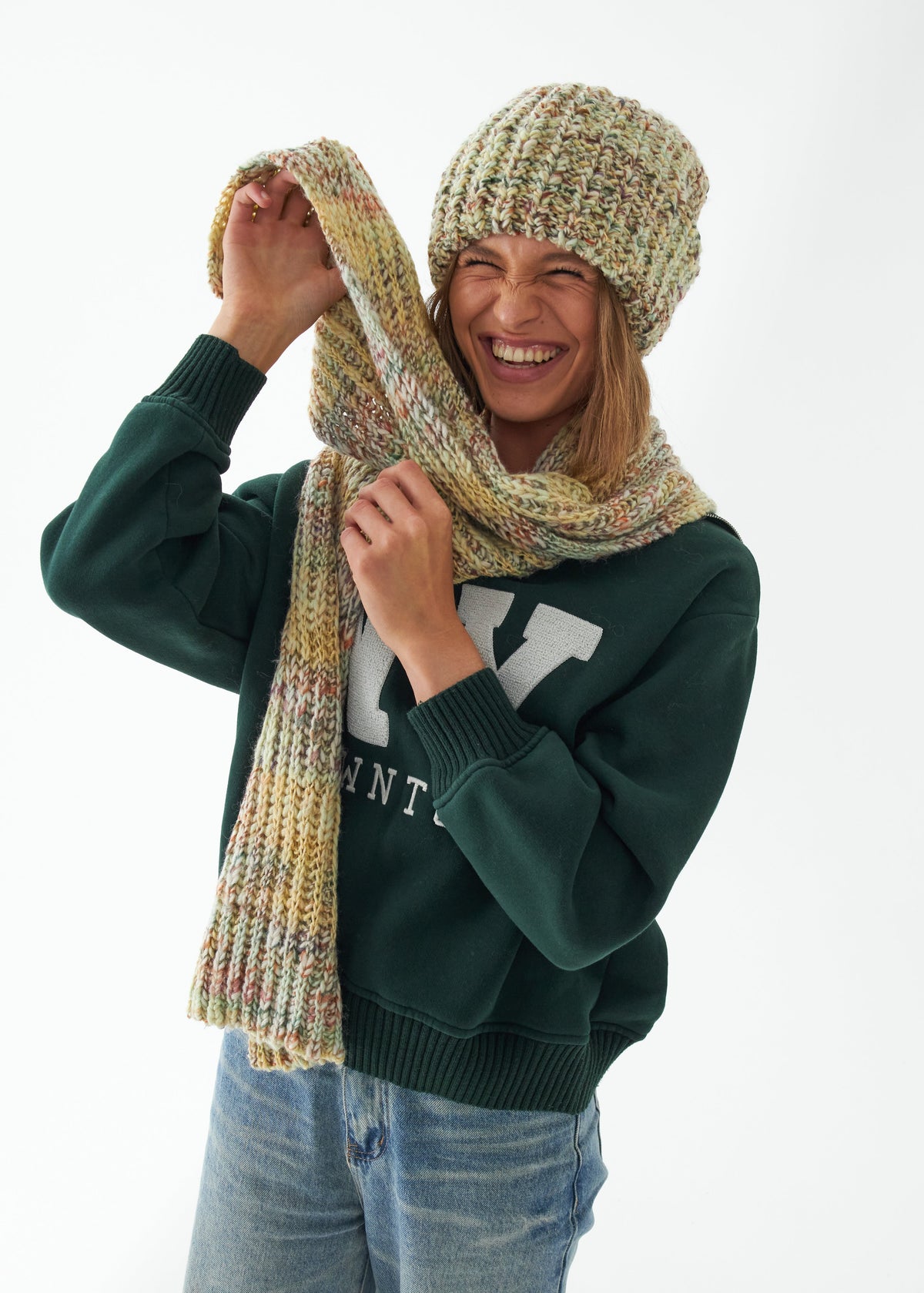 Oversized Yellow & Green alpaca-wool scarf: Smiling outfit view holding one end upward; beanie sold separately