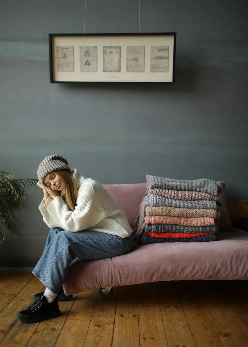 BRIKOLY London Gray & Beige knit beanie shown on a model seated on a sofa.