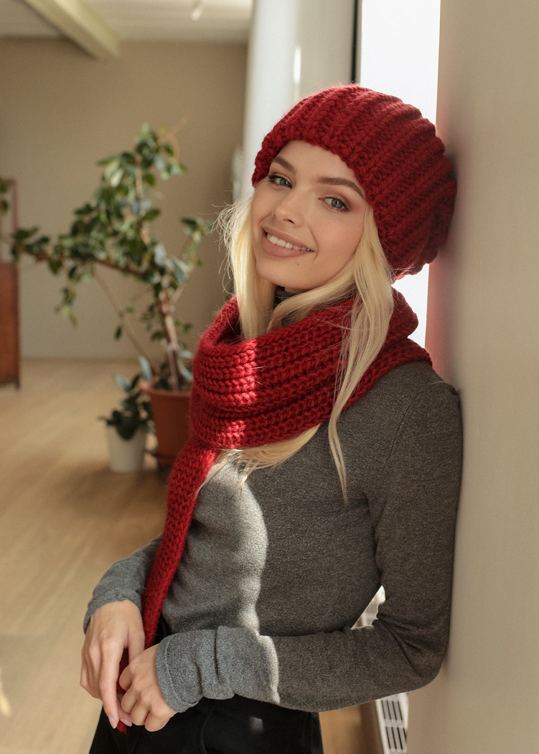BRIKOLY London Burgundy knit beanie worn by a seated model with a matching scarf.
