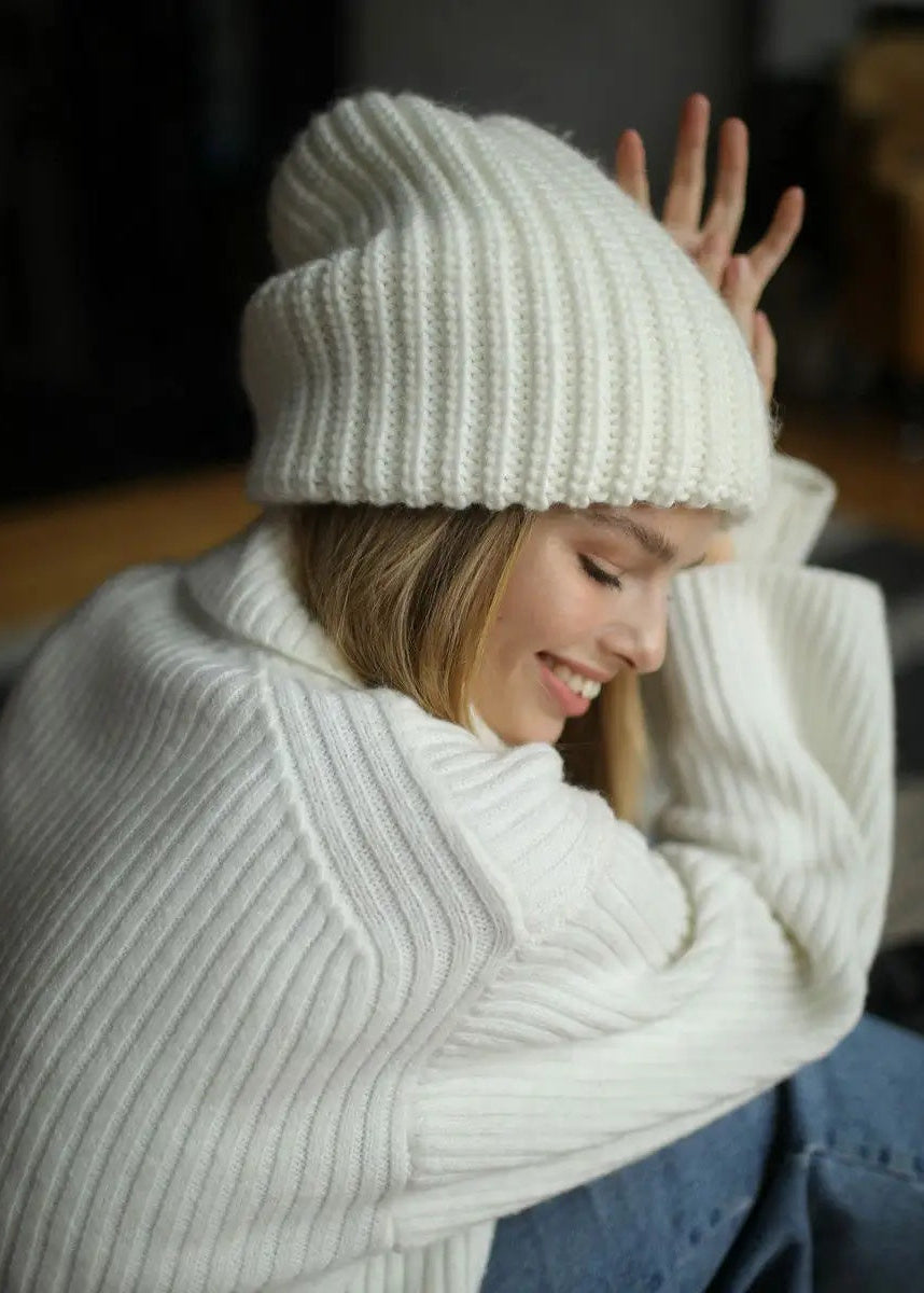 BRIKOLY London White knit beanie shown on a model looking down with her arms raised.