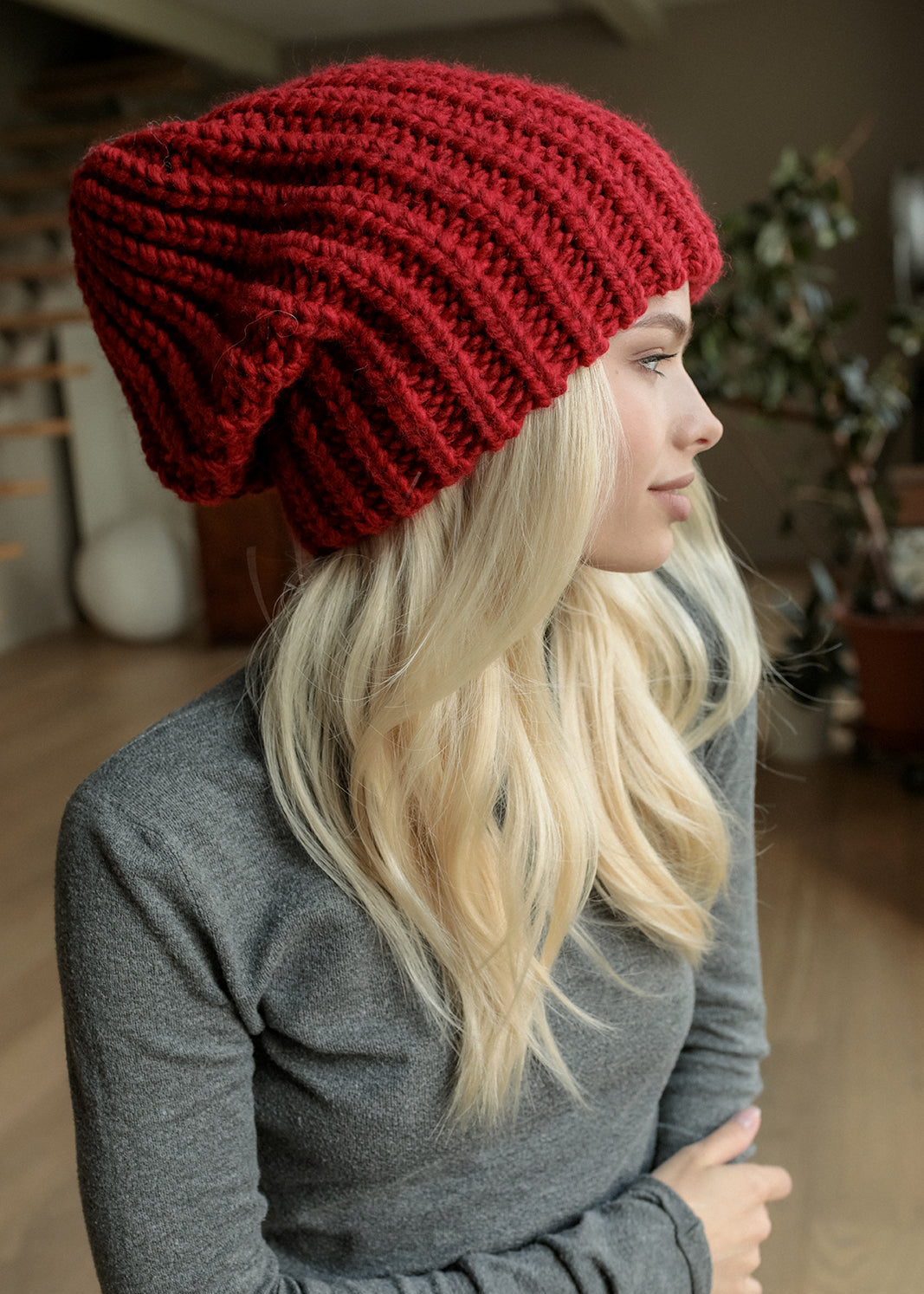 BRIKOLY London Burgundy knit beanie shown in profile on a seated model.