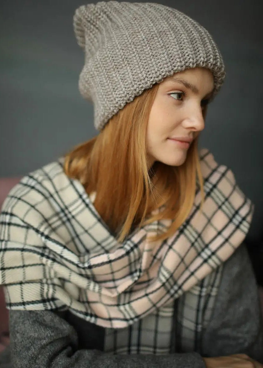 BRIKOLY London Gray & Beige knit beanie shown on a model looking to the side with a plaid blanket.