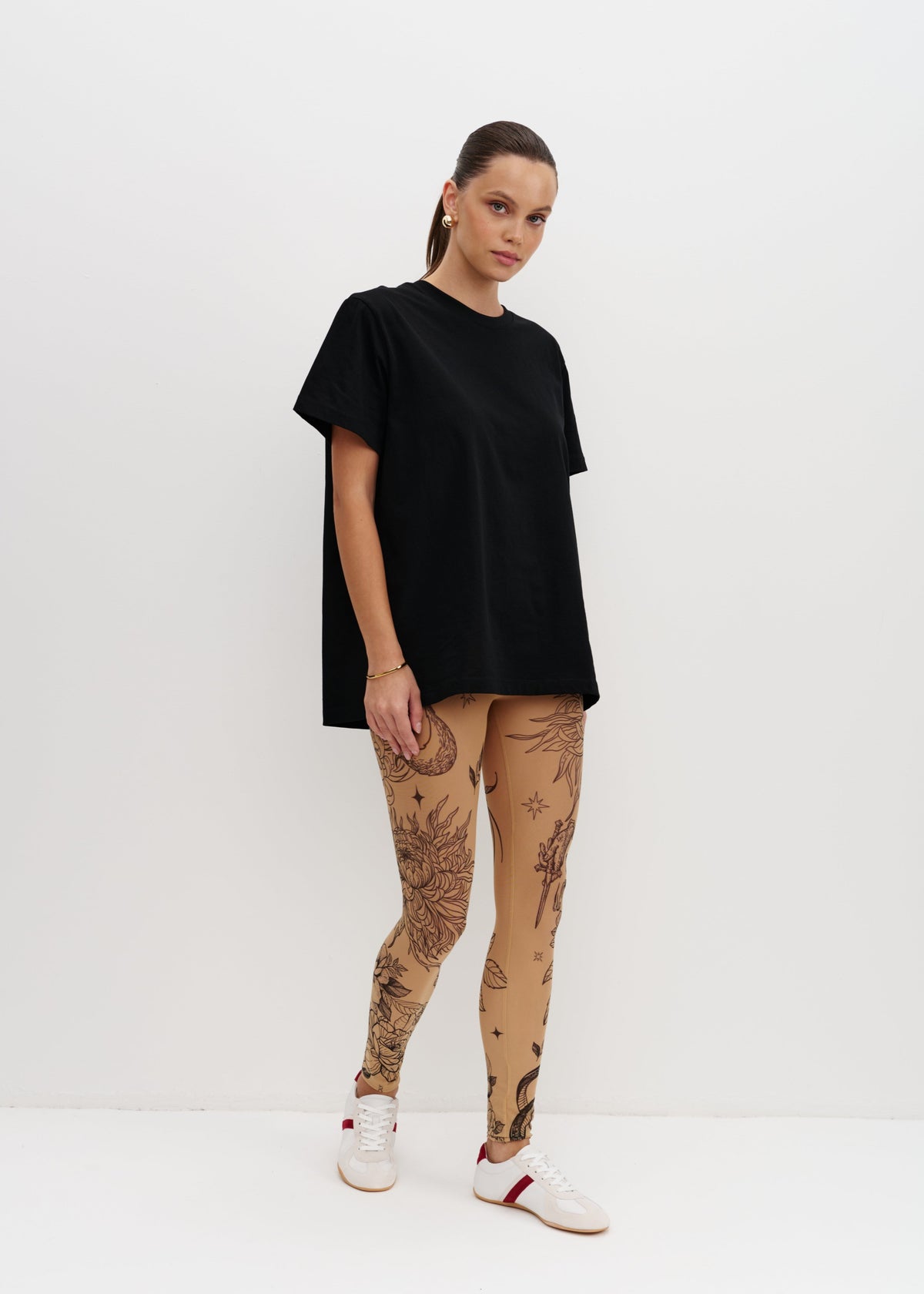 Person wearing a black t-shirt and beige leggings with tattoos on a white background