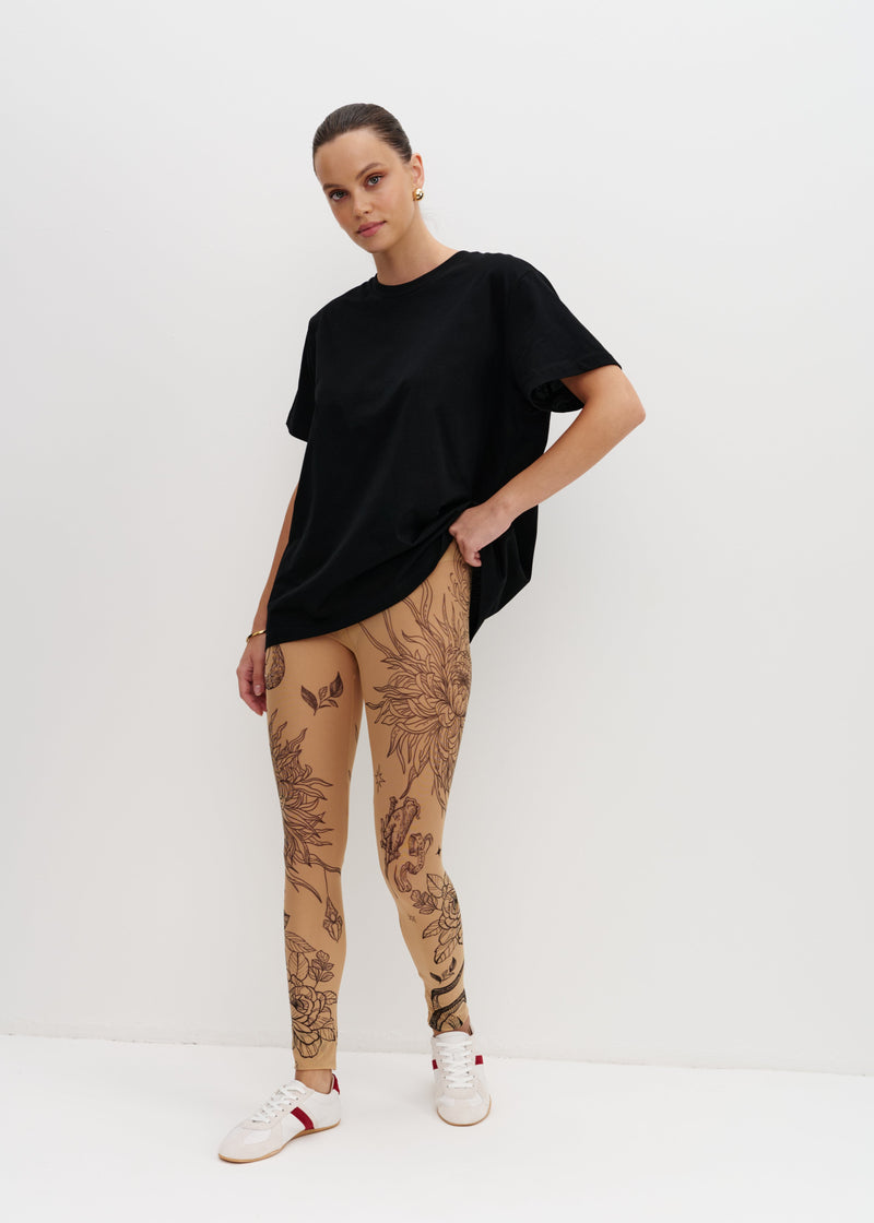 Person wearing a black oversized t-shirt and beige leggings with tattoos on a white background