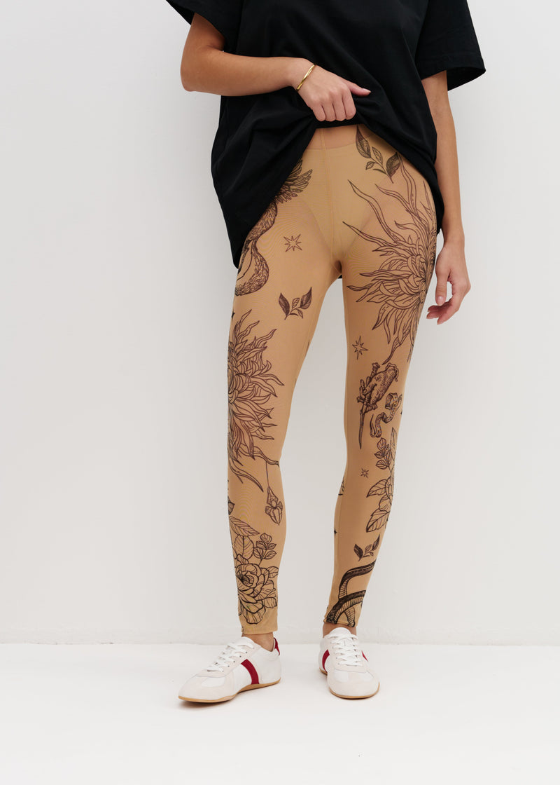 Person wearing tan leggings with black floral patterns on a white background