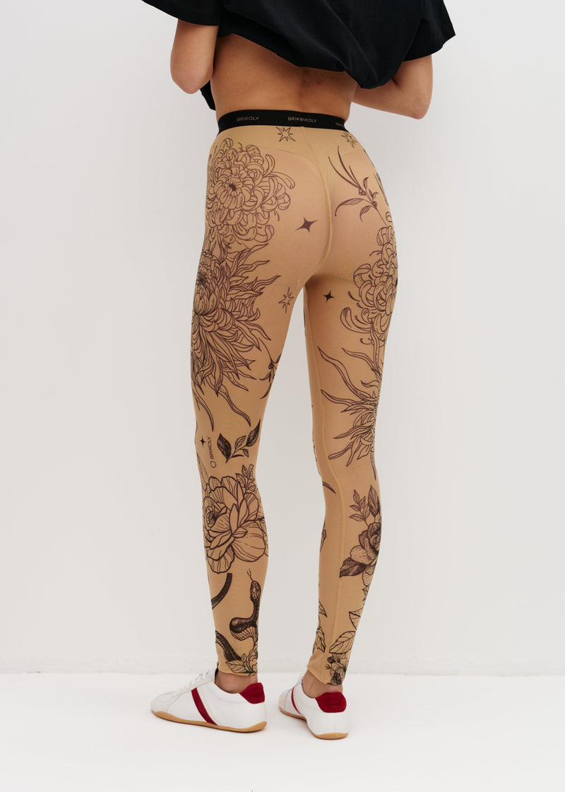 Person wearing beige leggings with black floral patterns on a white background