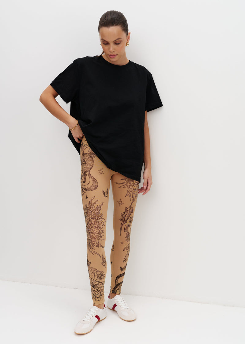 Person wearing a black t-shirt and beige leggings with tattoos on a white background