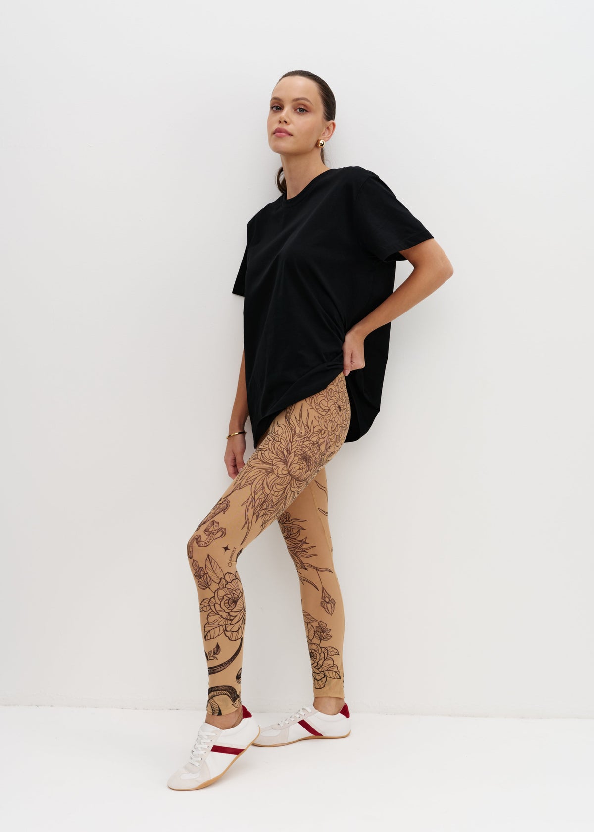 Person wearing a black t-shirt and beige leggings with patterns on a white background