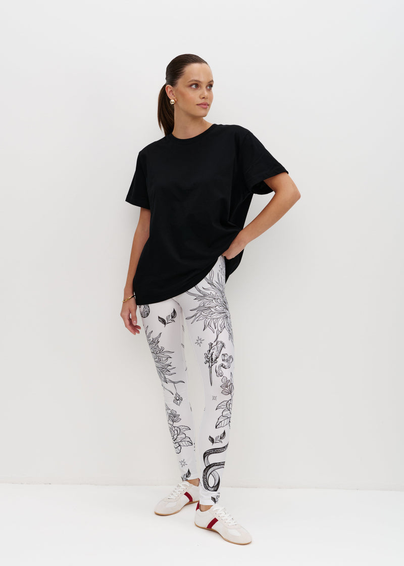 Woman wearing a black t-shirt and white leggings with black animal prints on a white background