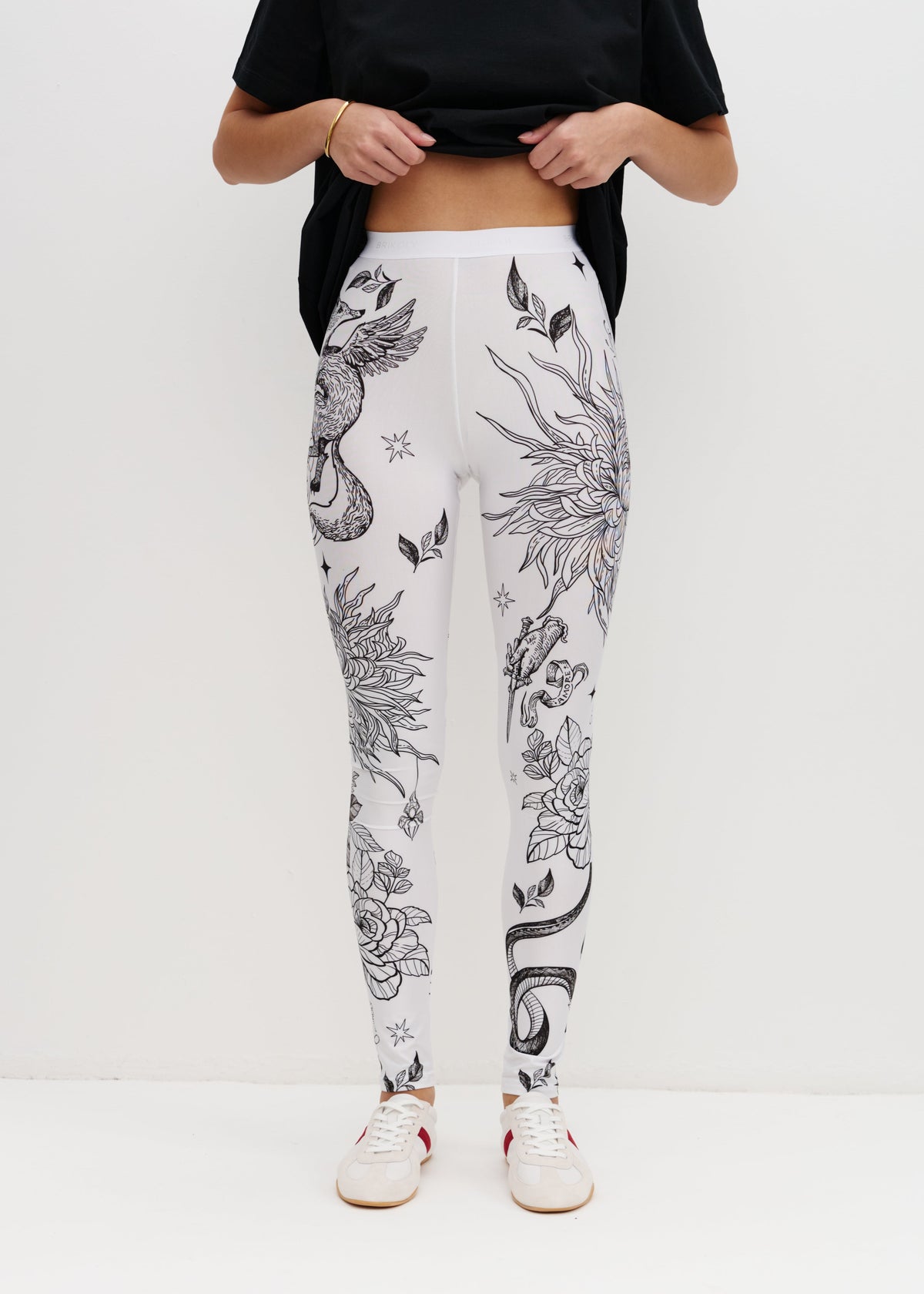 Person wearing white leggings with black floral patterns on a white background
