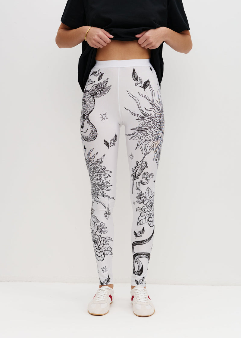 Person wearing white leggings with black floral patterns on a white background