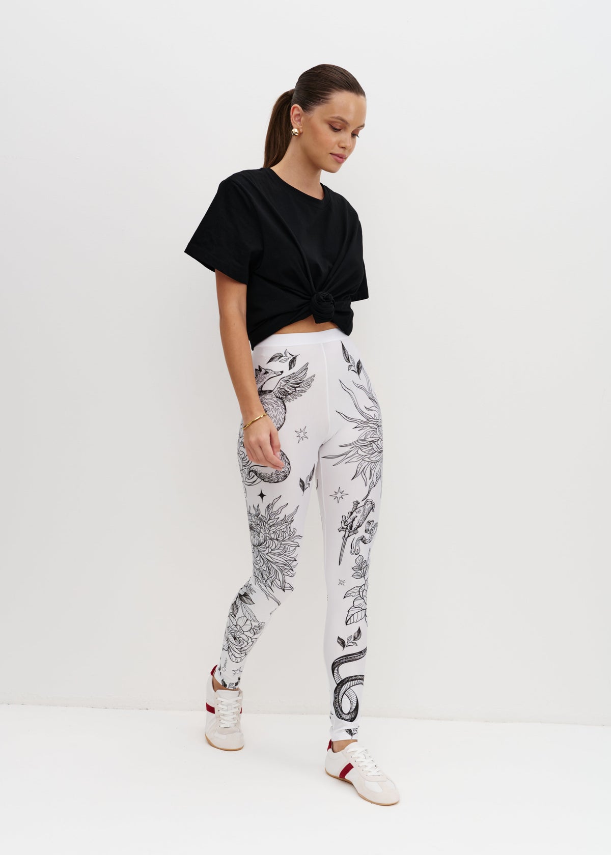 Woman wearing a black top and white pants with black floral patterns on a white background