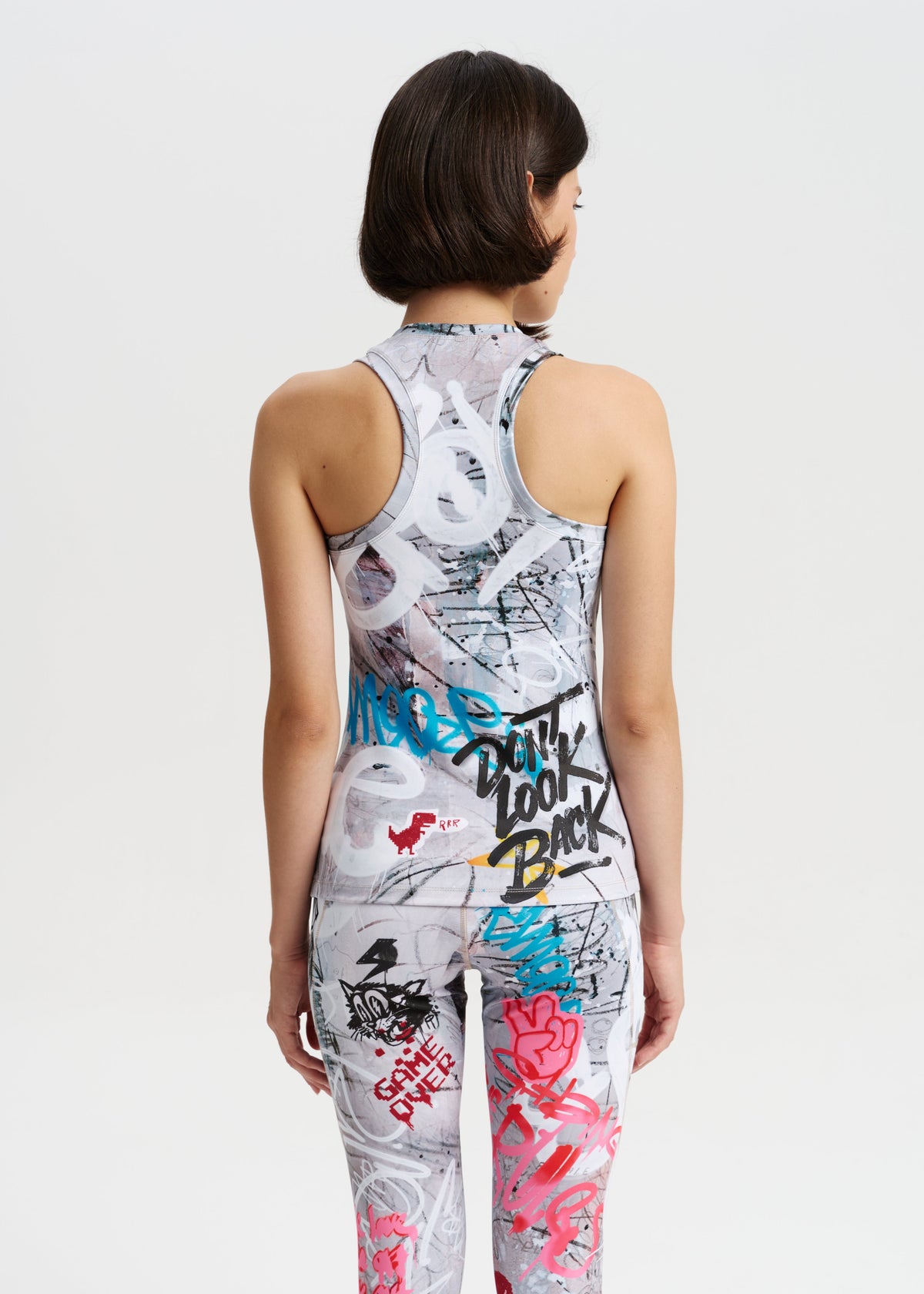 Person wearing a sleeveless top and pants with graffiti-style designs on a plain background