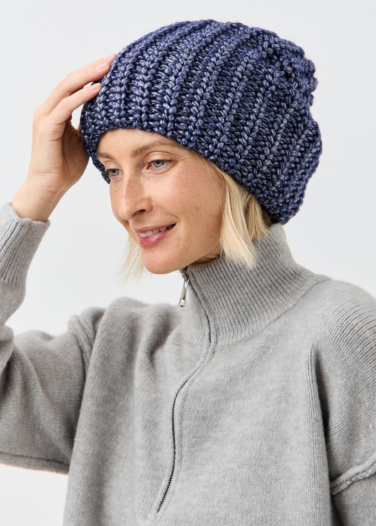 BRIKOLY Lustre Denim Melange oversized knit beanie worn by a model touching the brim.